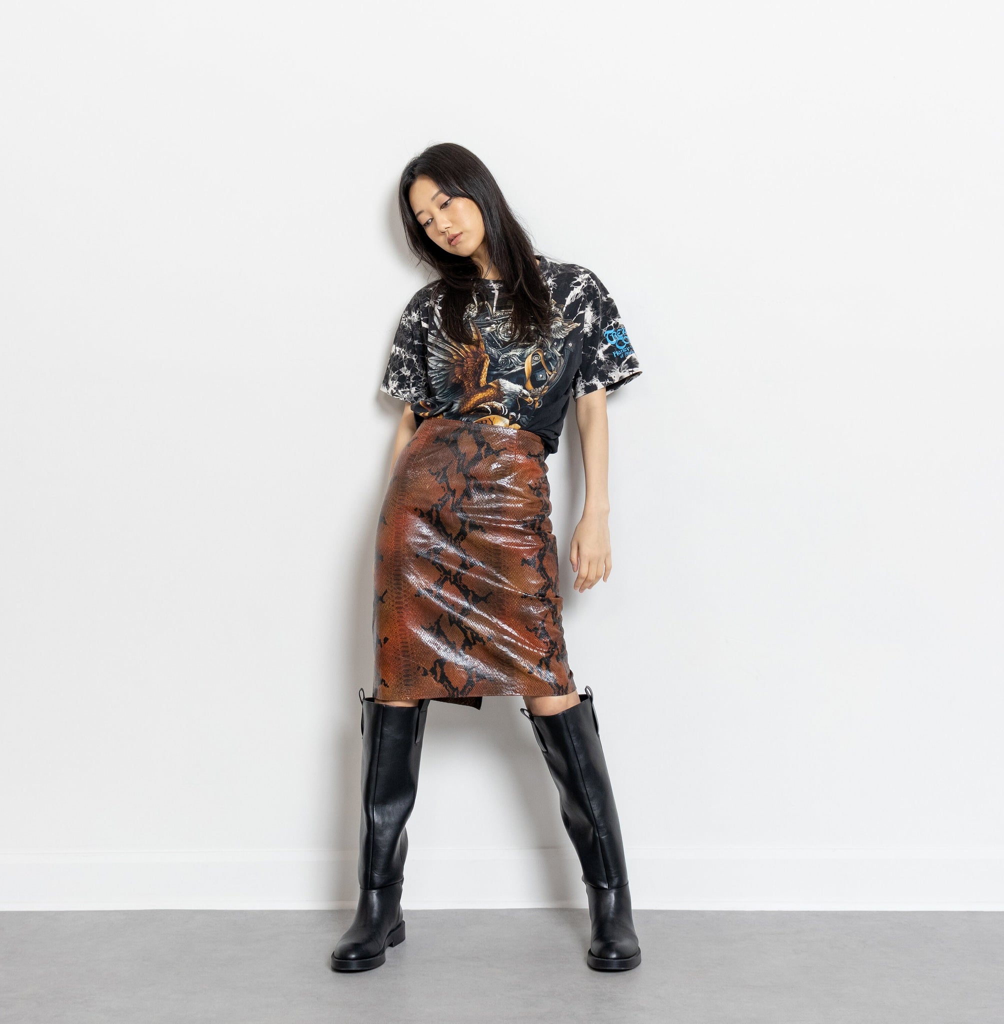 Person wearing a patterned top, brown leather skirt, and black knee-high boots on a white background