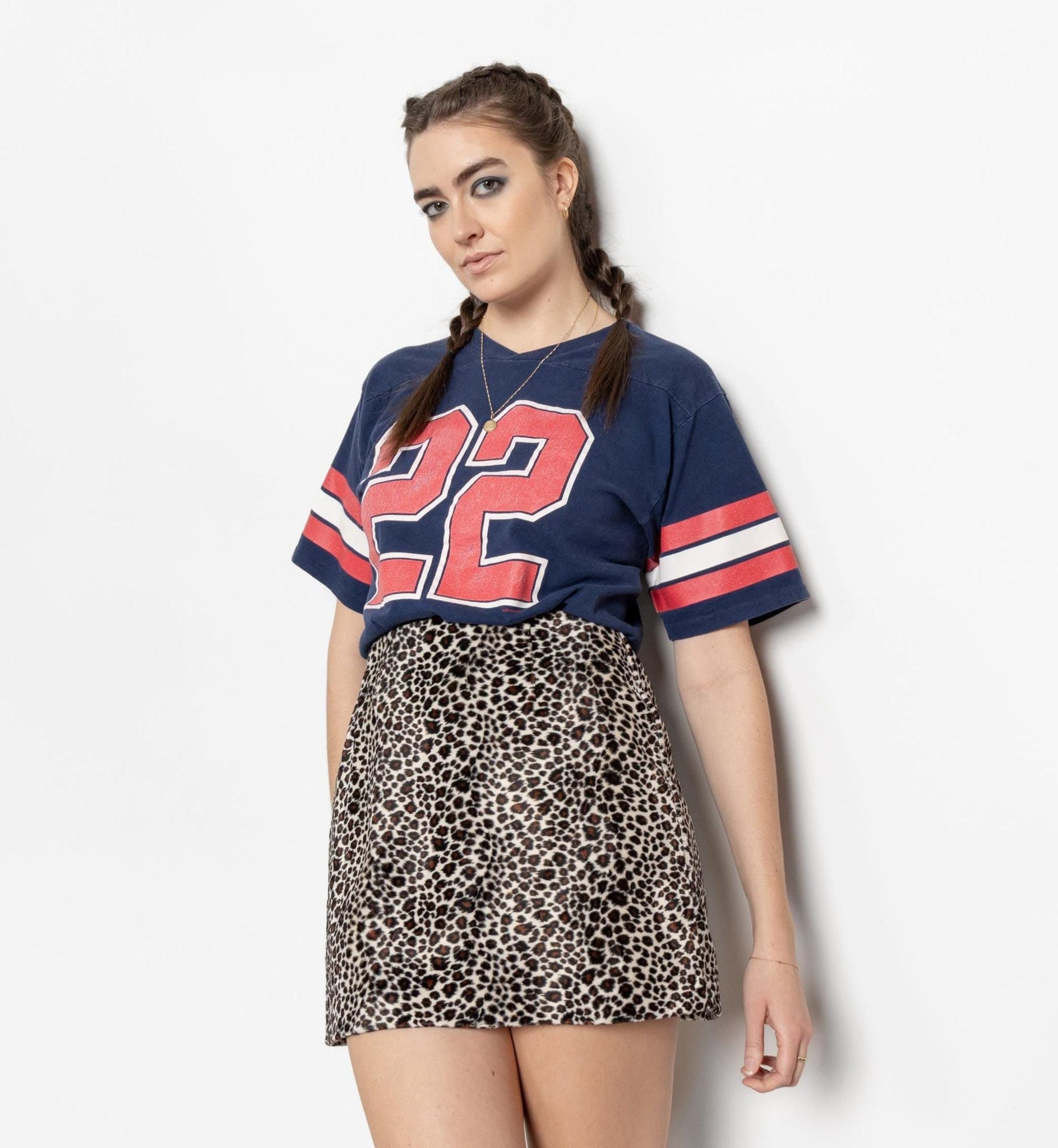 Woman wearing a blue sports jersey with red and white accents and a leopard print skirt on a white background