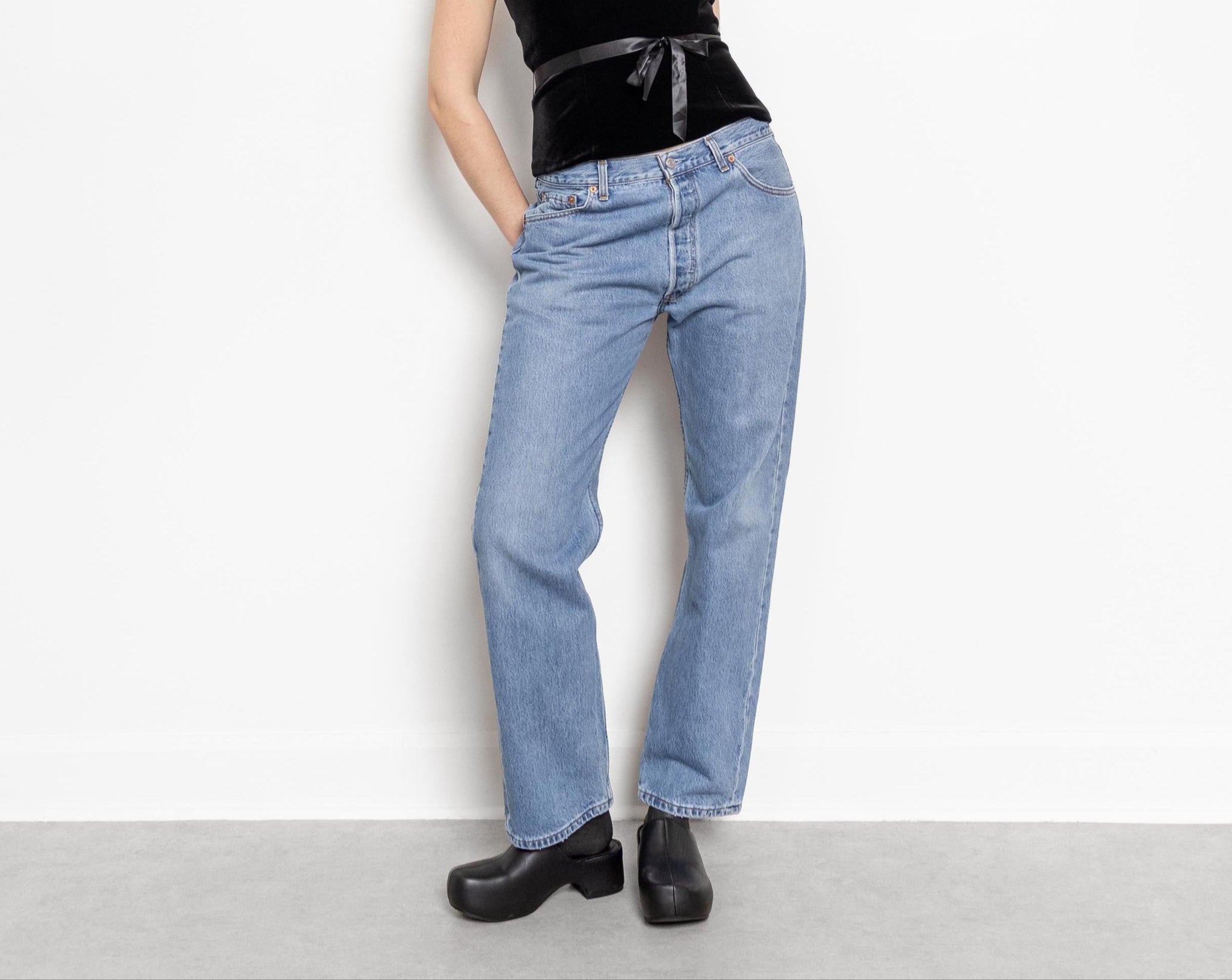 A person standing against a white background, wearing a black sleeveless top and blue straight-leg Levi's 501 jeans.