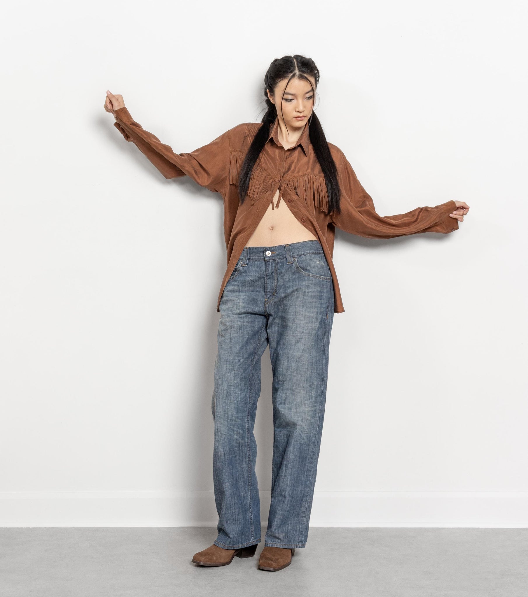 Person wearing a brown shirt and blue jeans against a white background