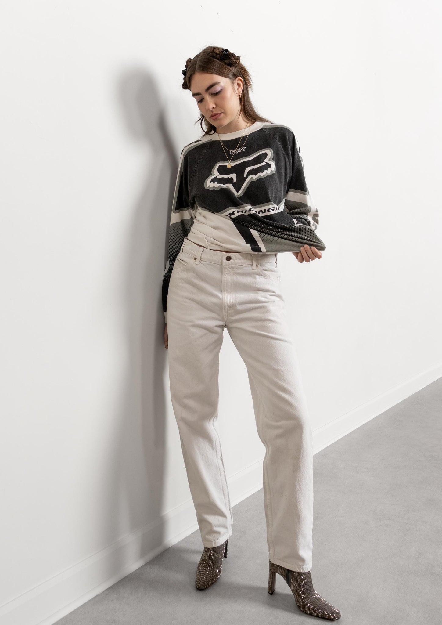 Person wearing a black and white sweater with a logo and white pants against a white wall.