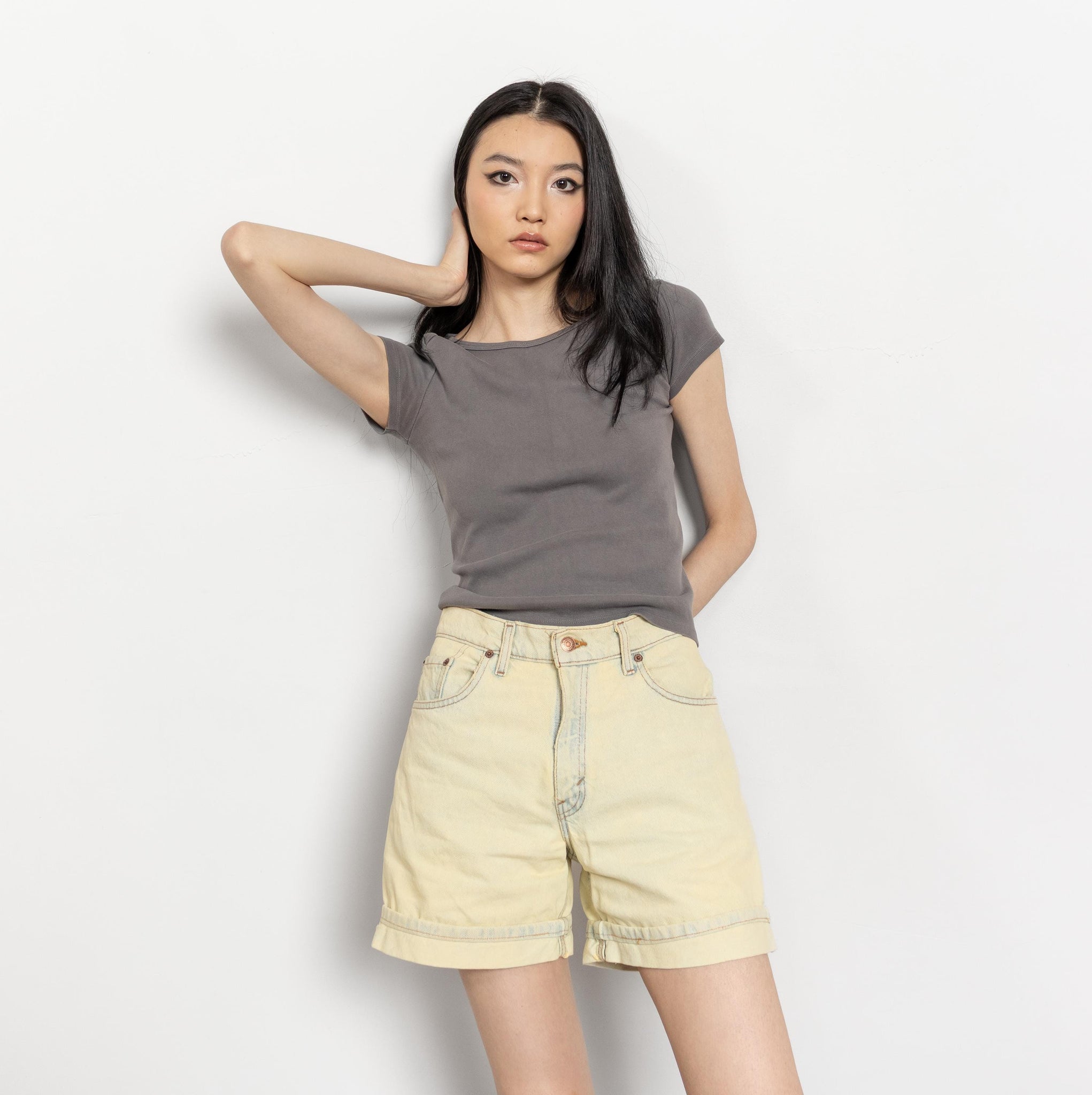 Woman wearing a gray t-shirt and light yellow shorts on a white background