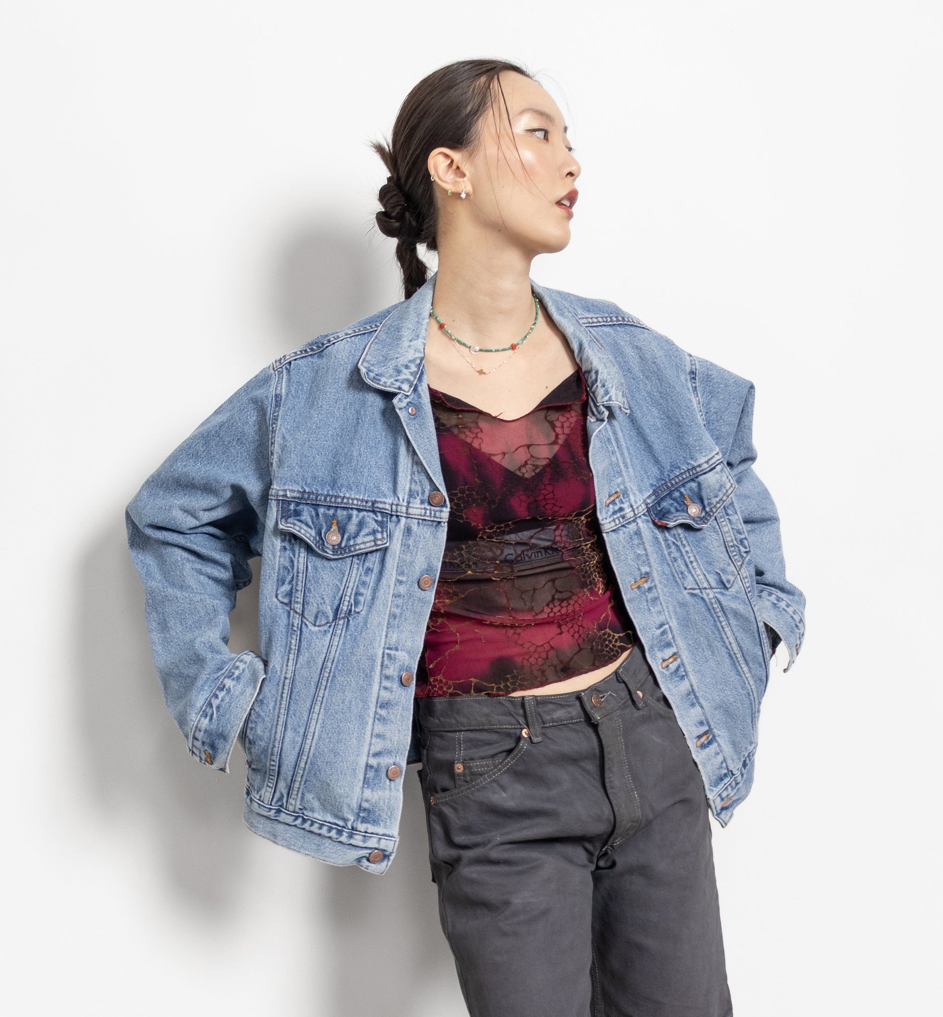 Person wearing a denim jacket, red top, and gray shorts against a white background