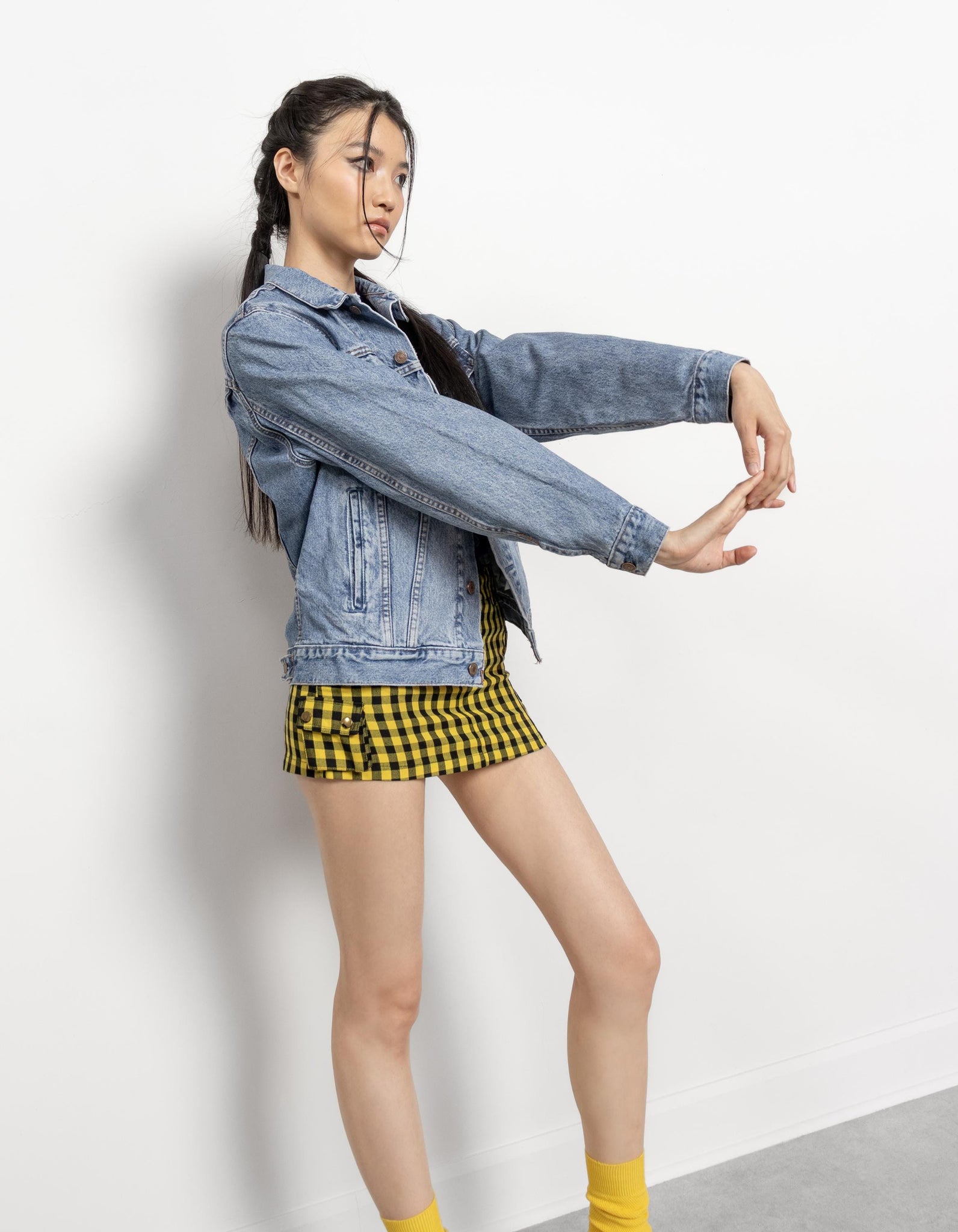 Woman wearing a denim jacket and checkered skirt on a plain background