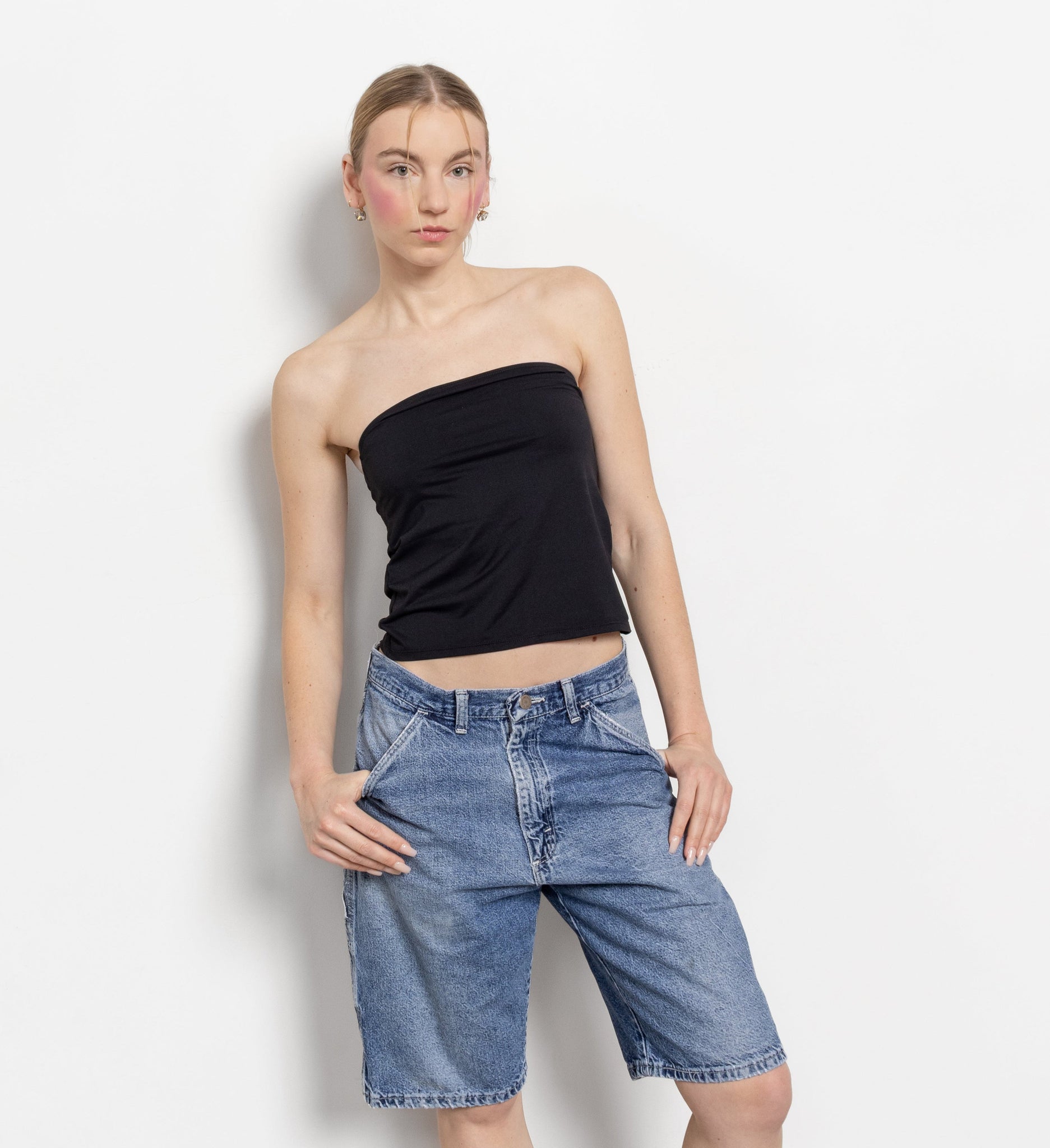Person wearing a black strapless top and denim shorts against a white background