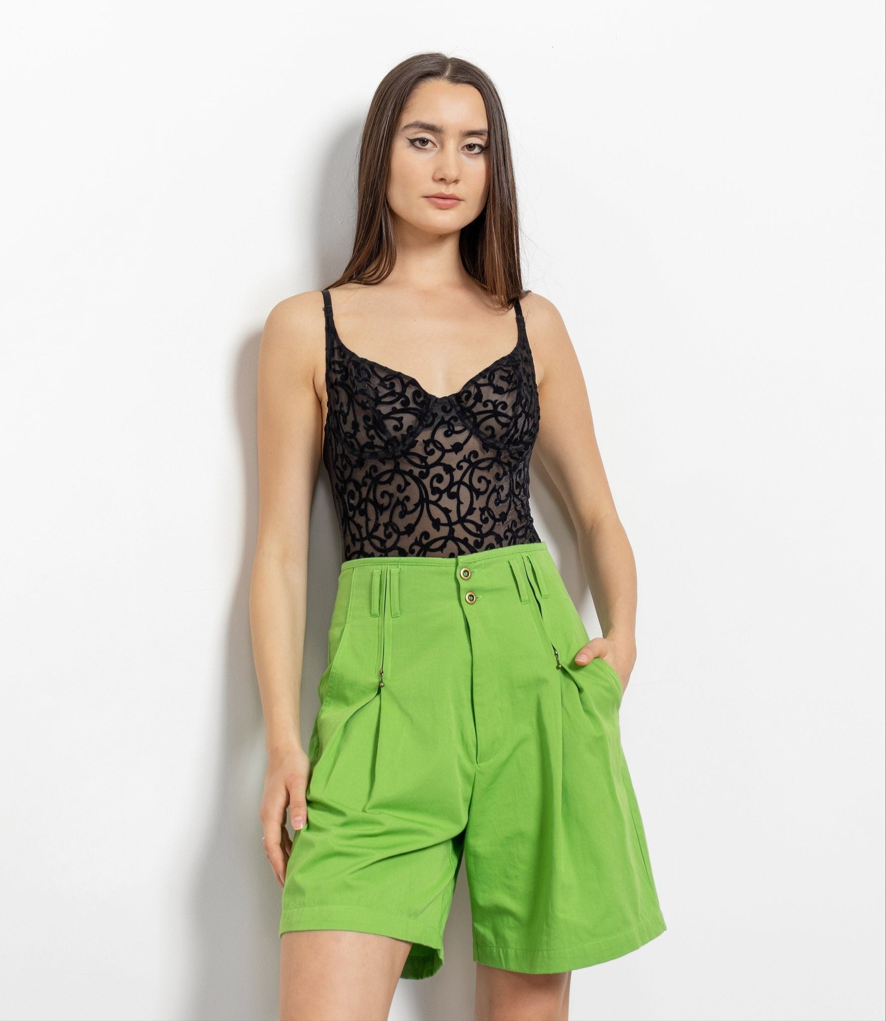 Woman wearing a black lace top and green shorts against a white background