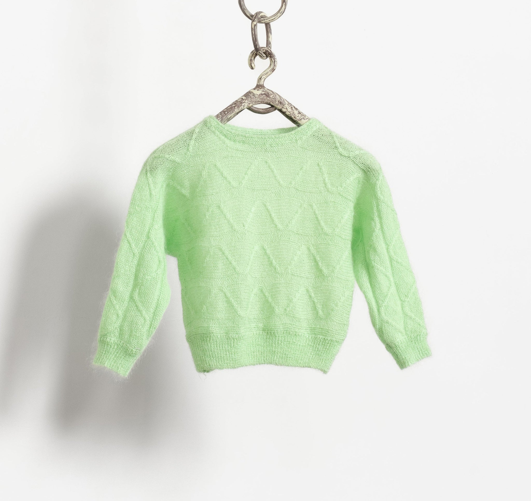 A vintage 80's mohair blend loose knit sheer pullover sweater in mint green color, featuring batwing sleeves and a shorter cropped fit, hanging from a chain.