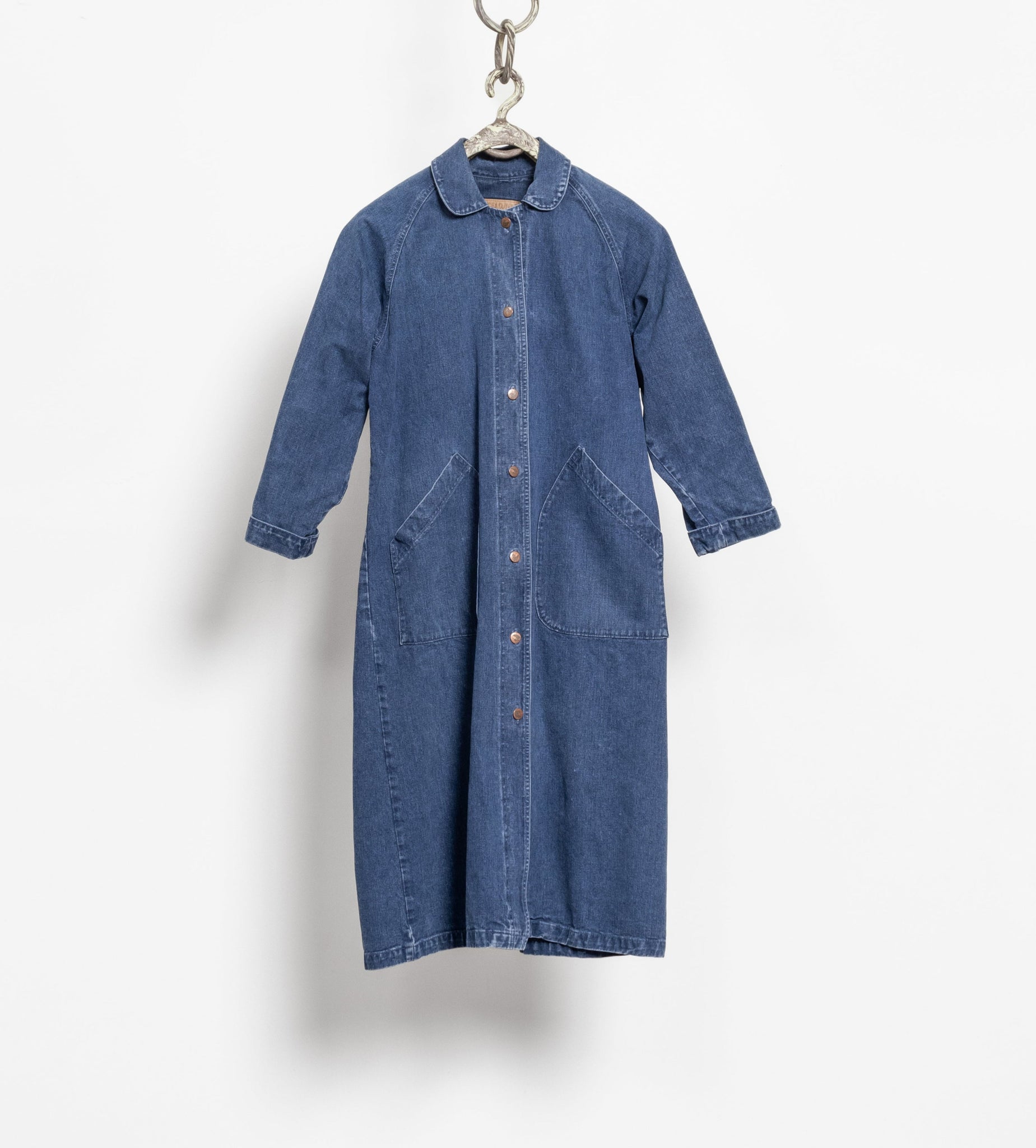 A long dark blue denim jacket with a relaxed fit, buttons down the front, and two front slit pockets, displayed hanging against a white background.