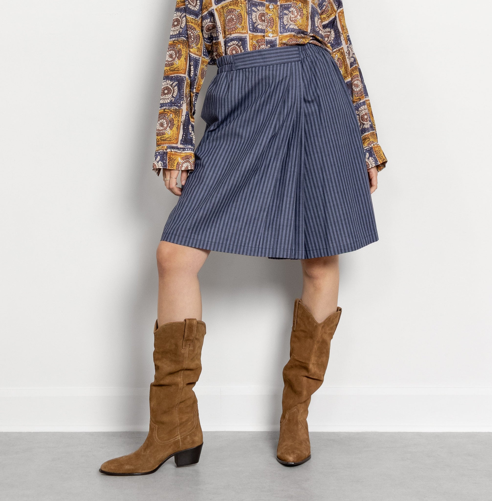 Woman wearing a patterned blouse, blue skirt, and brown knee-high boots on a white background