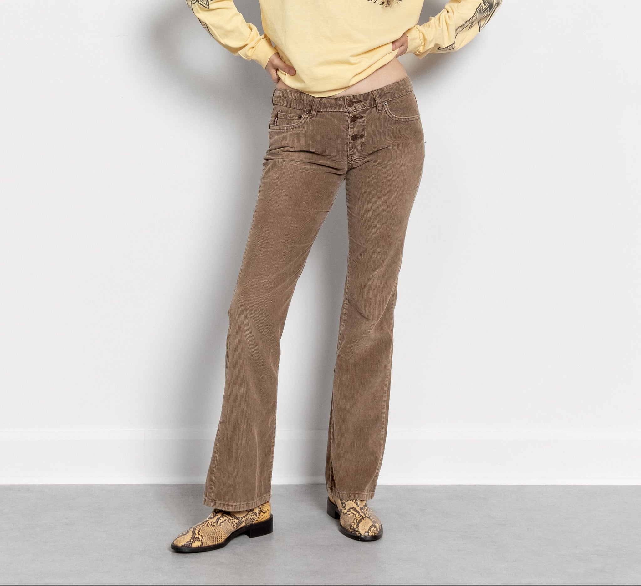 Woman wearing a yellow graphic sweatshirt and brown pants against a white background