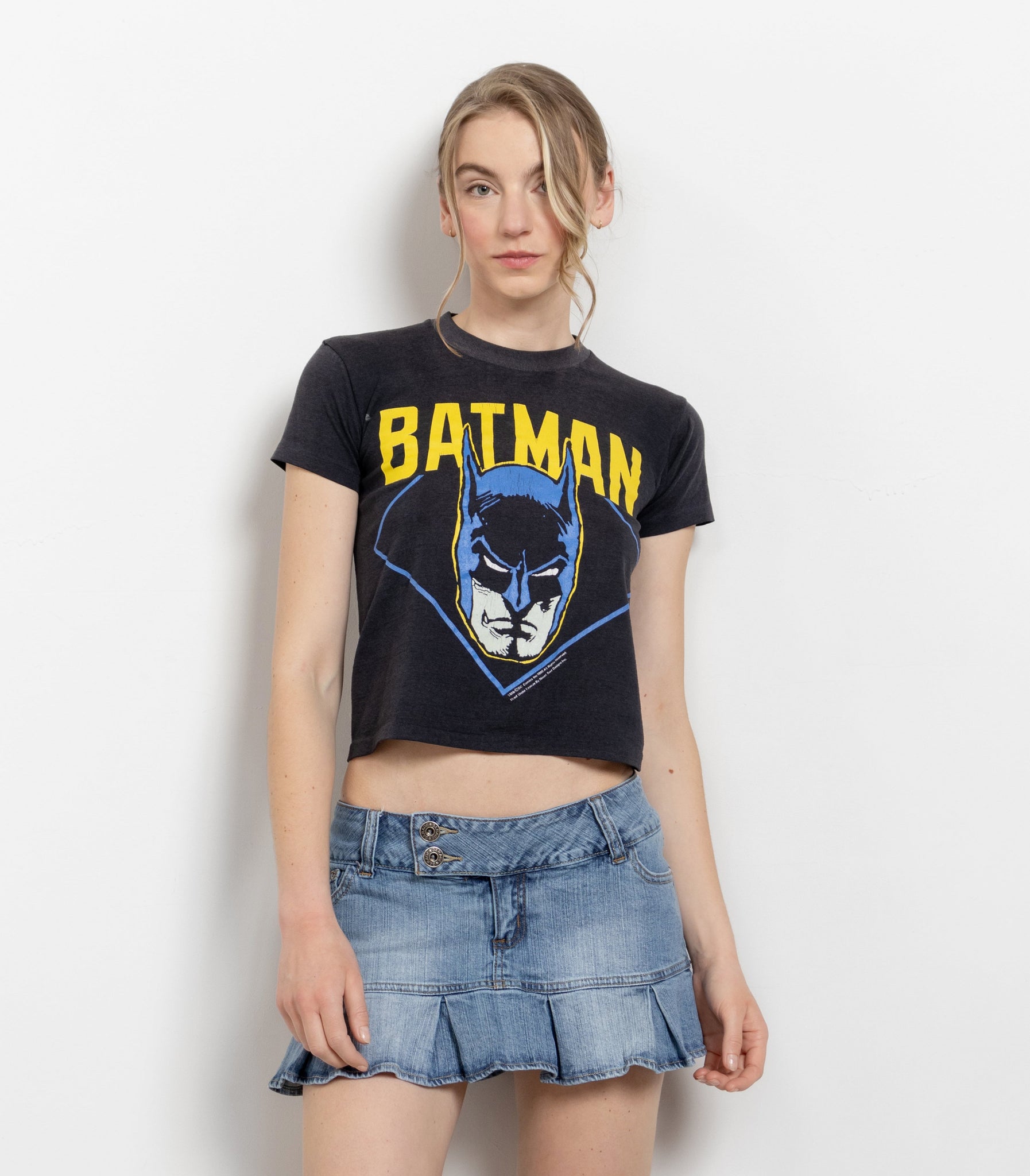 A person wearing a black crop t-shirt with a Batman graphic and a denim mini skort.