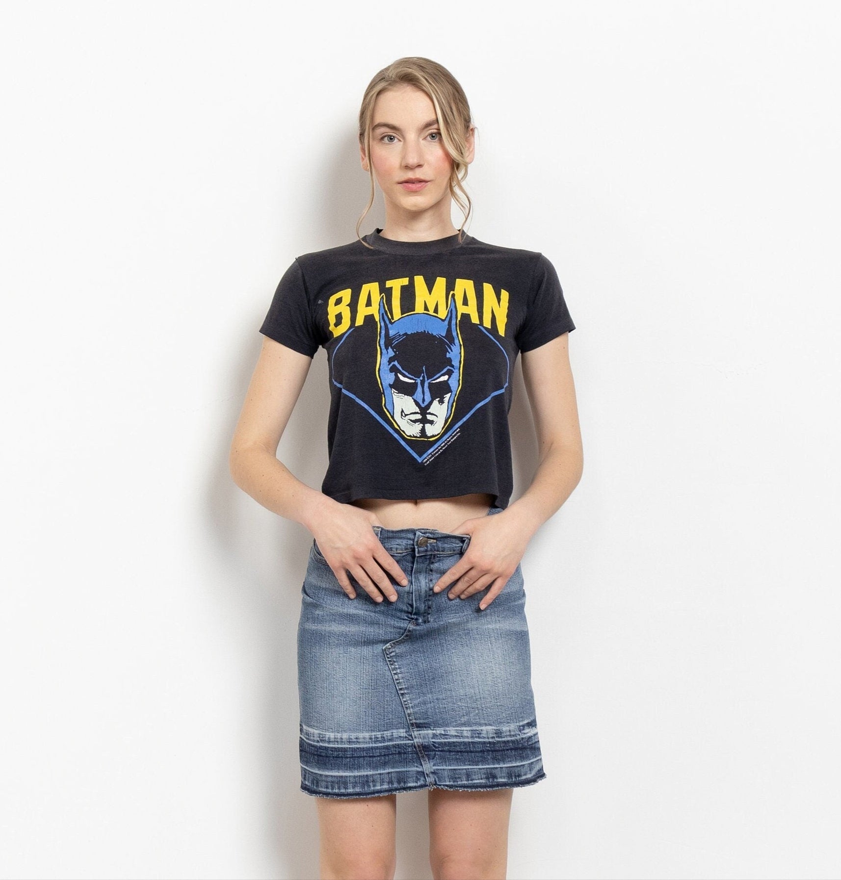 A woman posing with a vintage 2000's Batman t-shirt and a low-rise denim mini skirt.