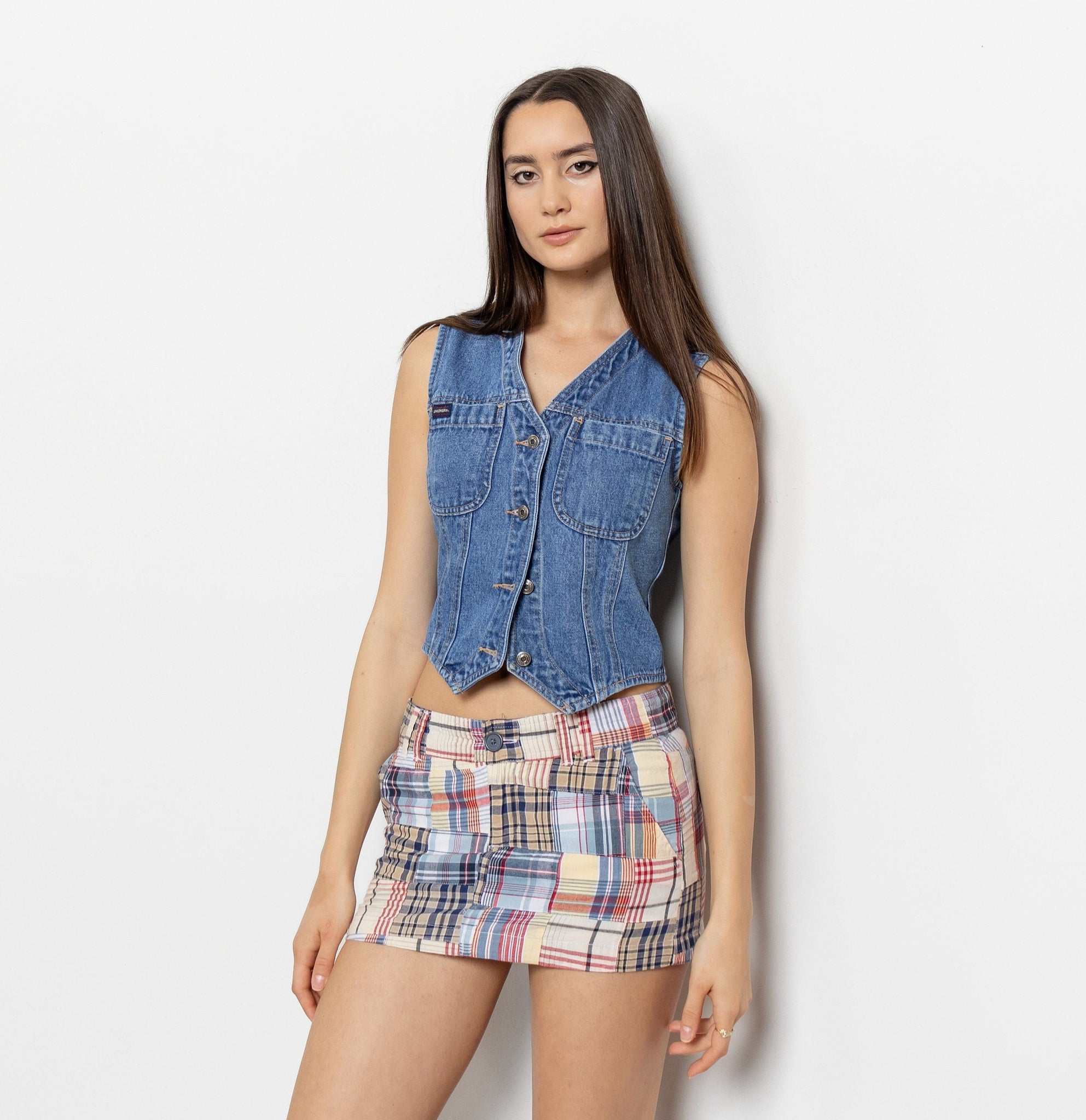 Woman wearing a denim vest over a plaid skirt on a white background
