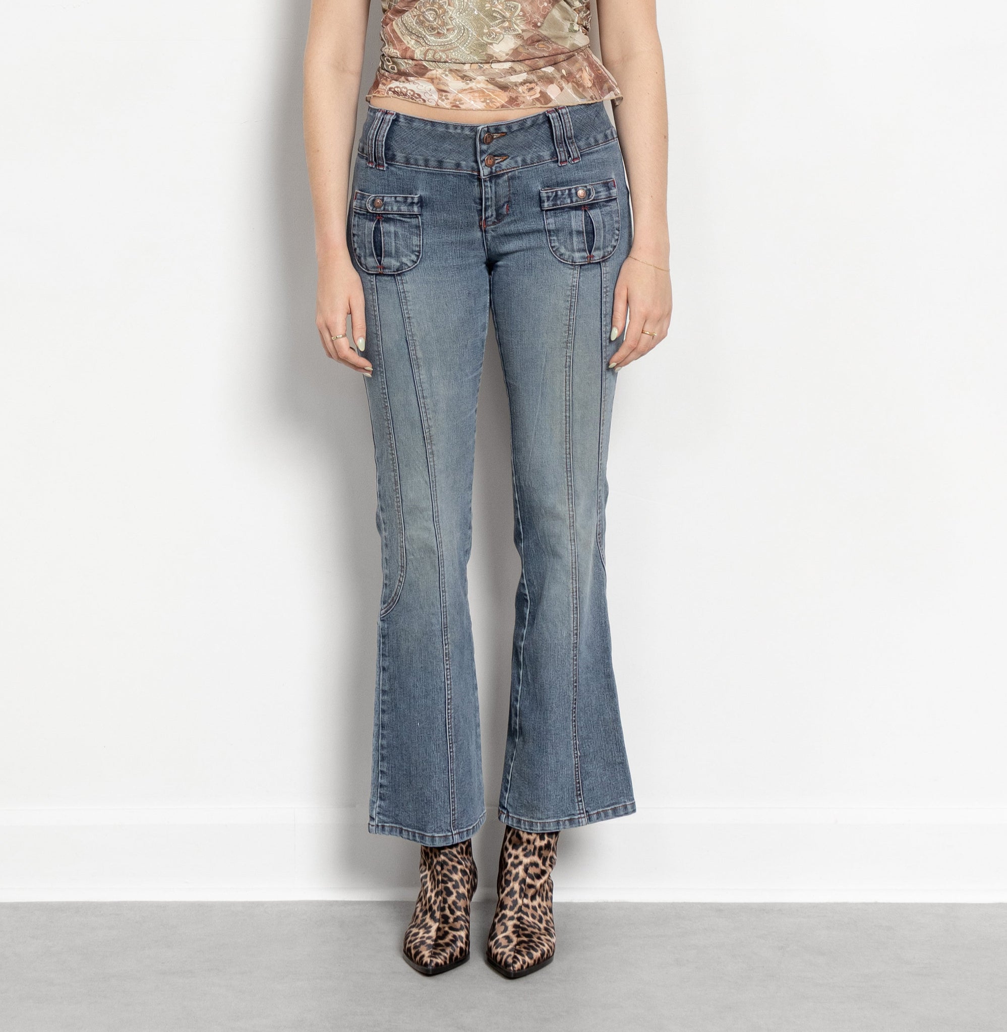Woman wearing a patterned top and blue jeans on a white background