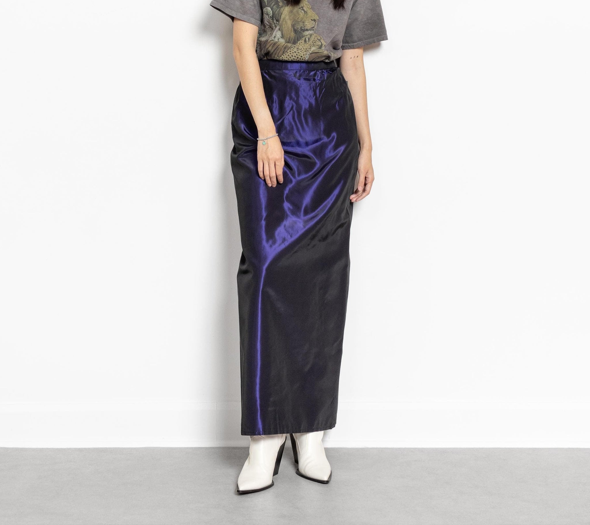 A person wearing a vintage 90's purple metallic high rise maxi skirt with a shimmery finish, paired with a gray top and white boots.