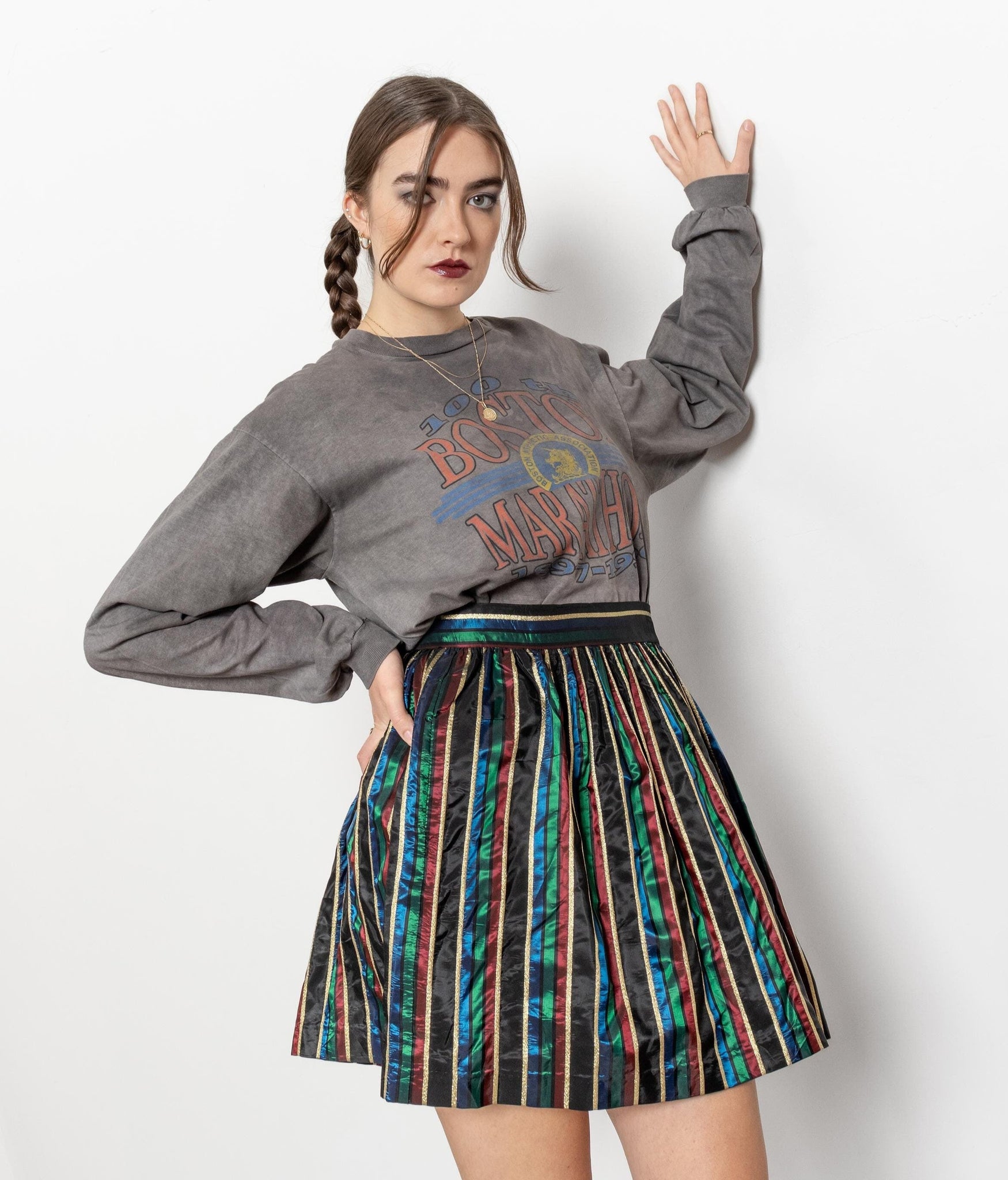 Woman wearing a gray sweatshirt with colorful text and a striped skirt on a white background