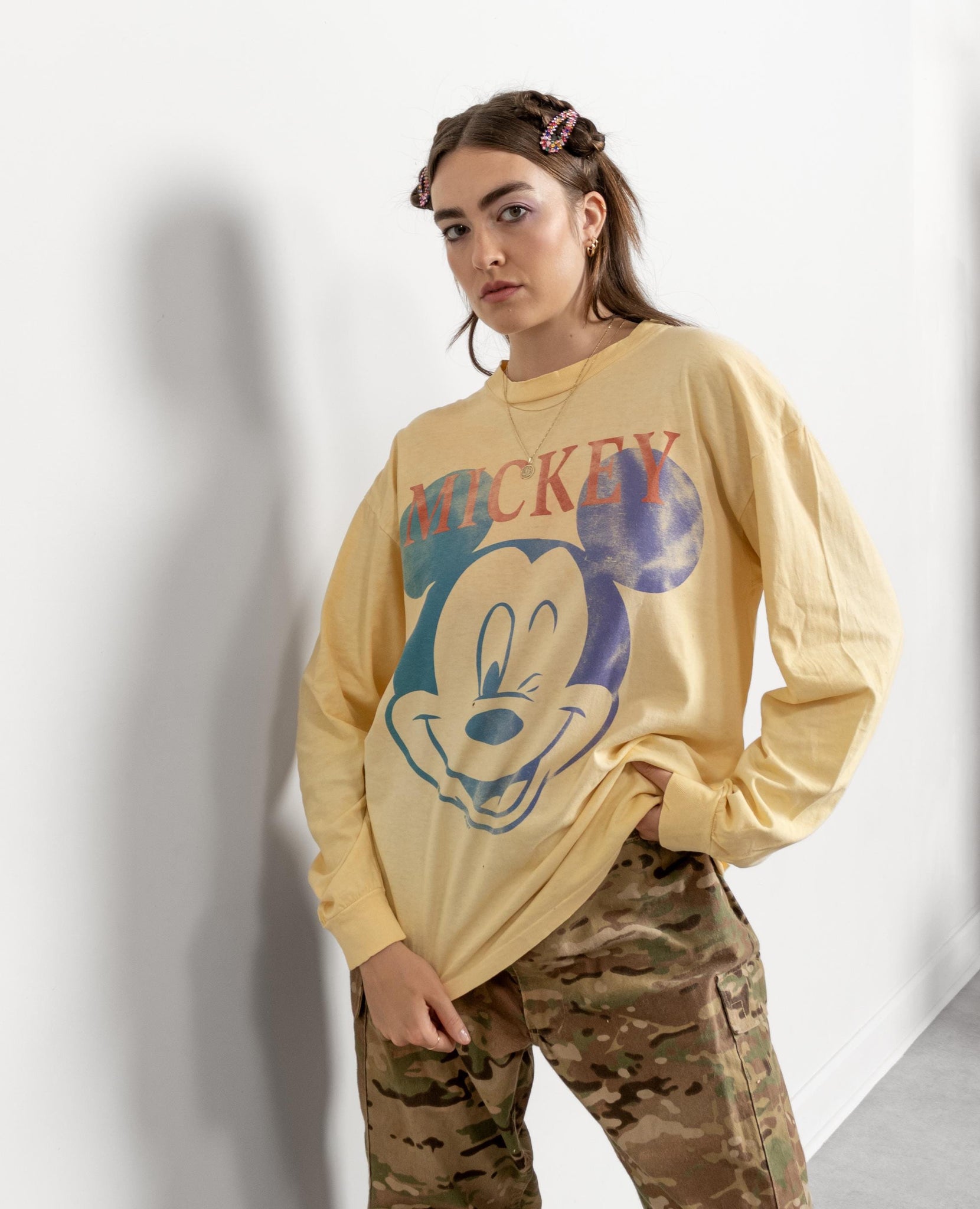 Person wearing a yellow long-sleeve shirt with a Mickey Mouse graphic and camouflage pants on a white background