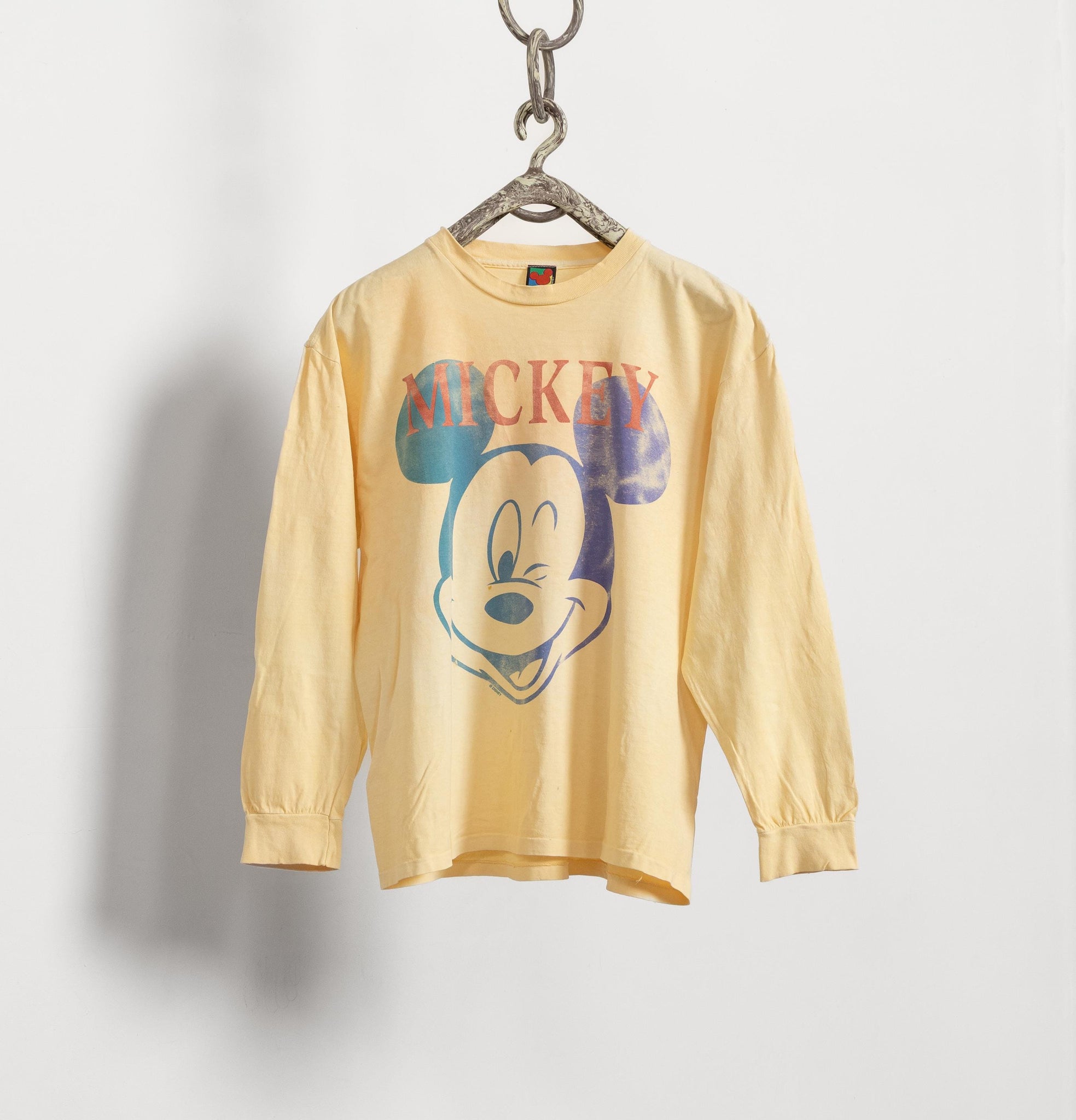 Yellow long-sleeve shirt with a Mickey Mouse graphic on a hanger against a white background