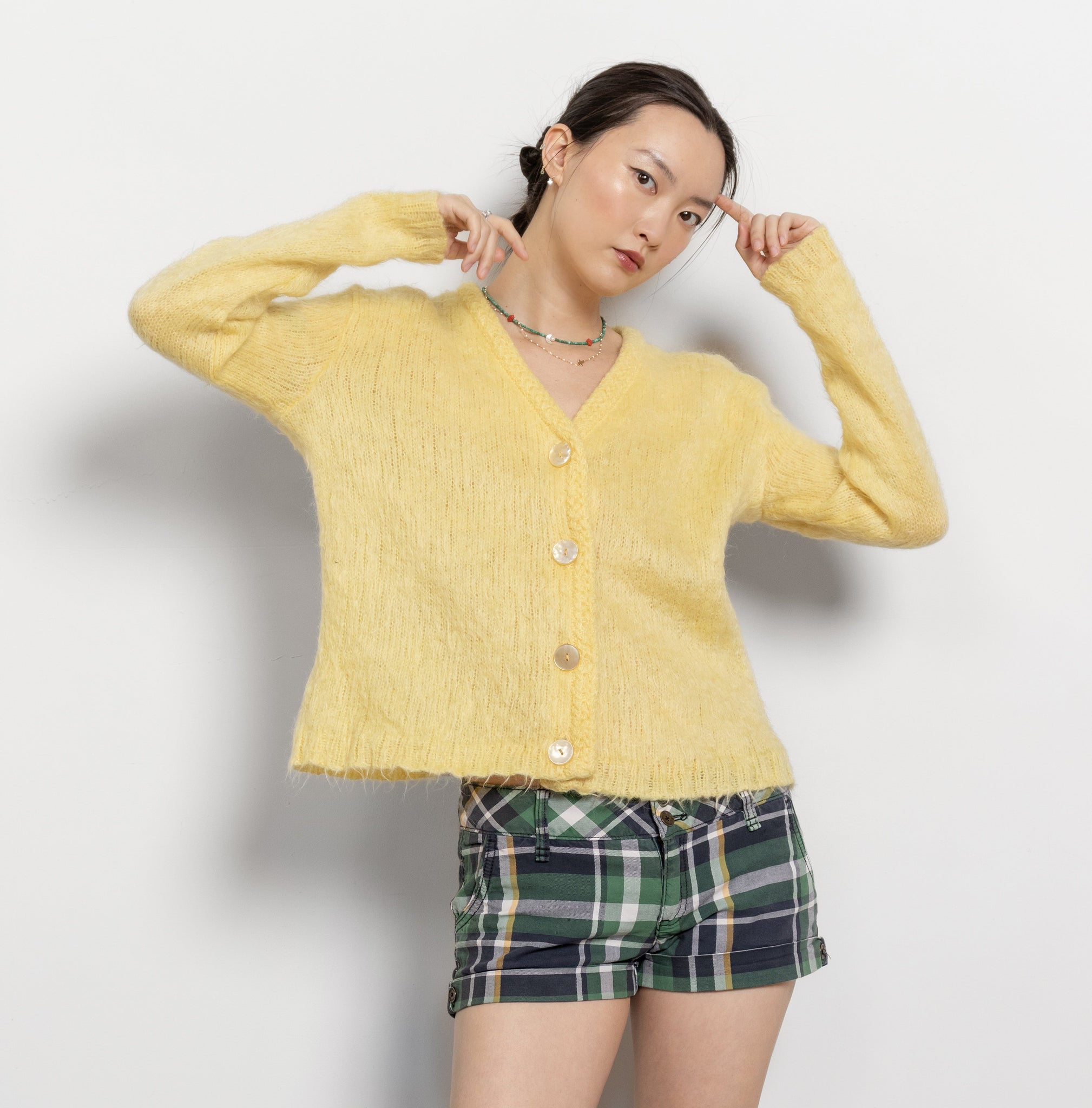Person wearing a yellow cardigan and plaid shorts on a white background