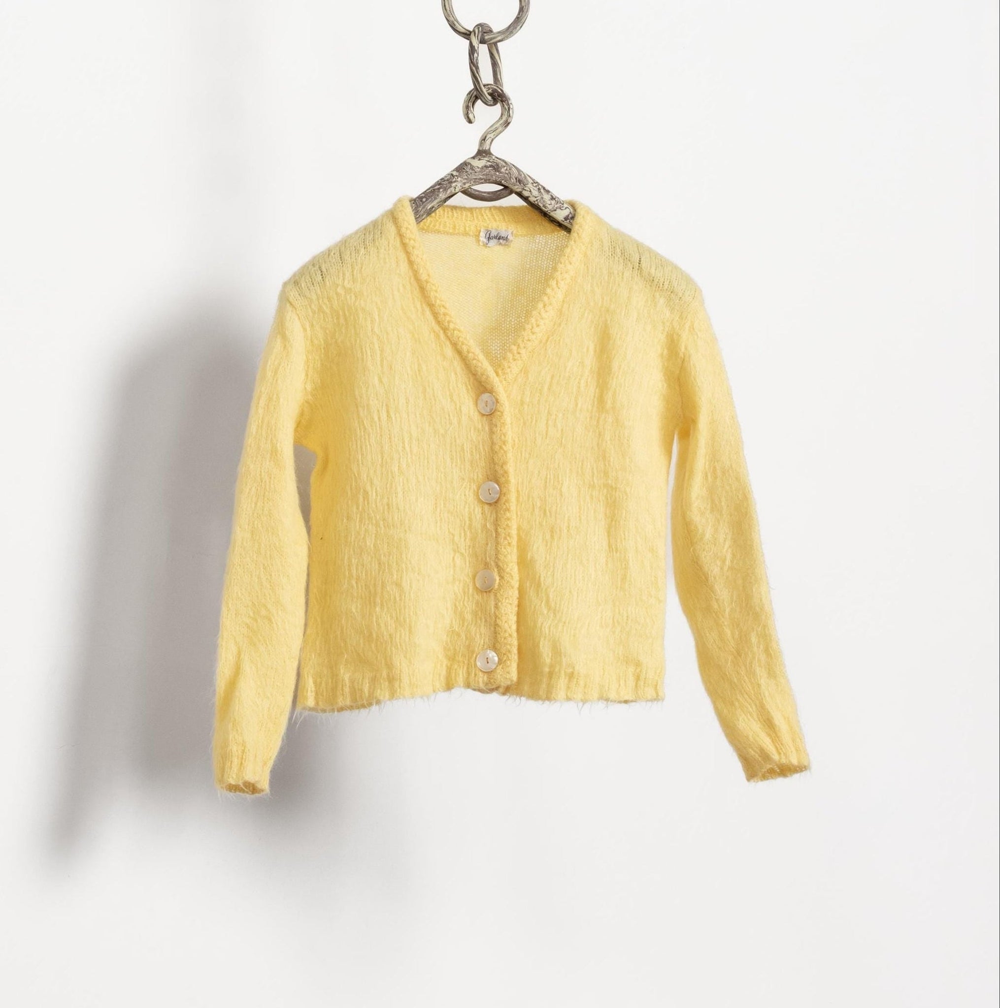 Yellow cardigan on a hanger against a white background