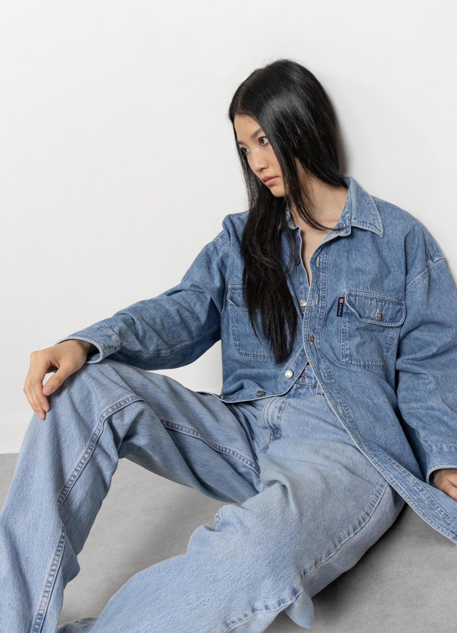 Person wearing a denim outfit sitting on a gray surface with a white background