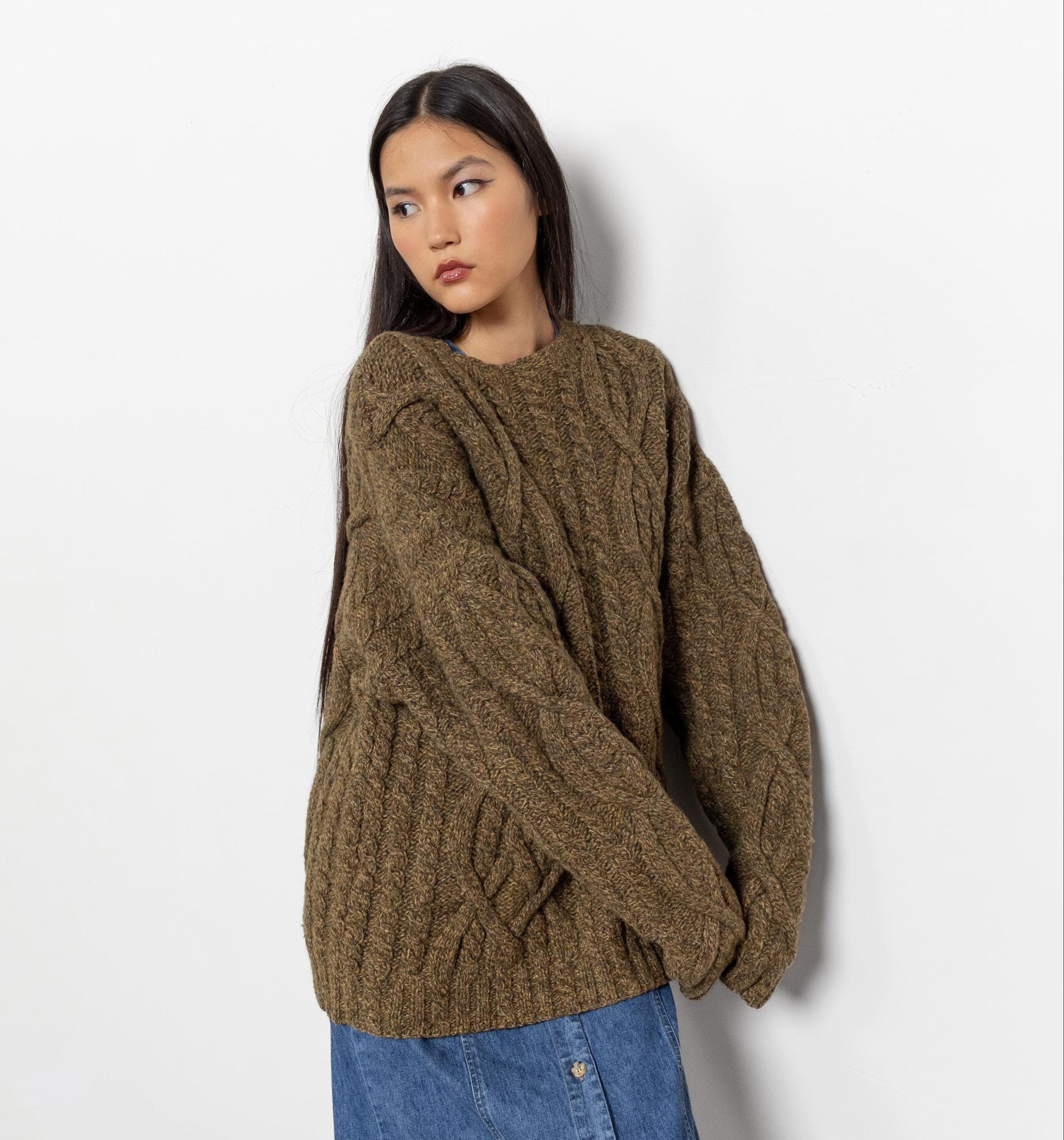 Woman wearing a brown oversized sweater and blue jeans against a white background