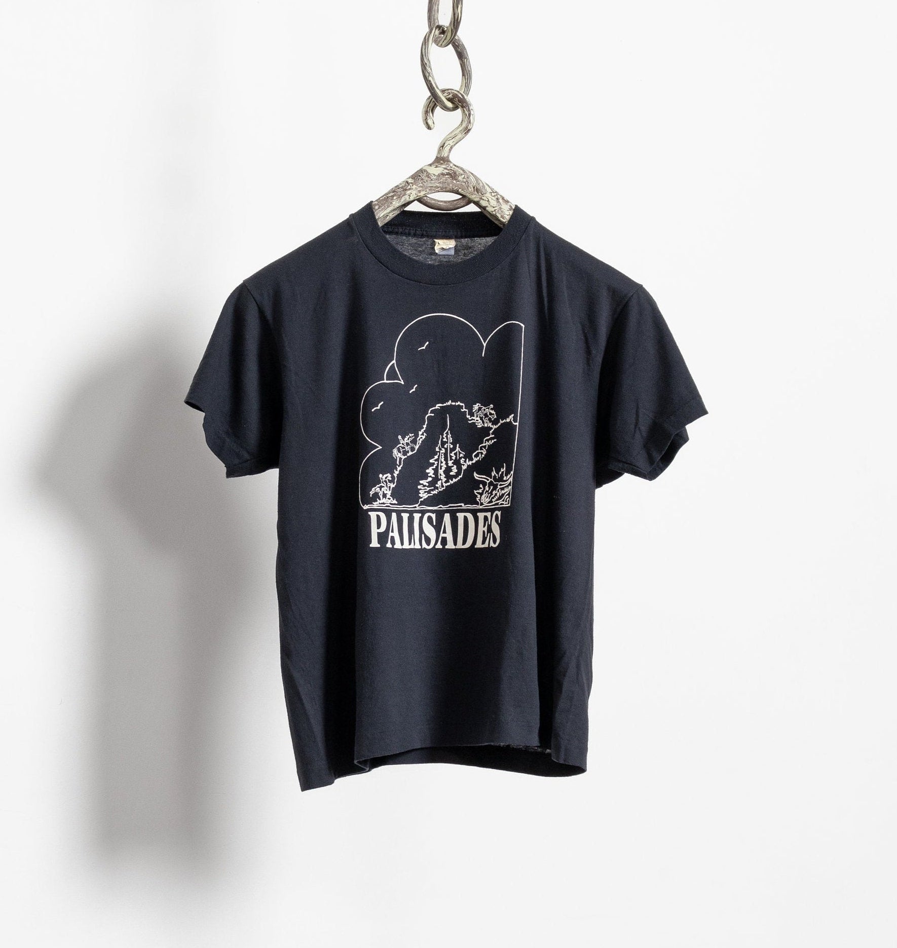 A black Palisades crewneck t-shirt hanging against a white background, displaying a graphic print in the center.