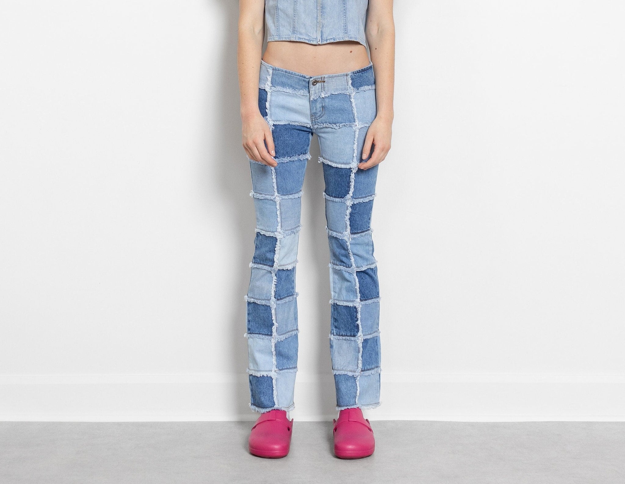 A person standing against a white background, wearing low rise patchwork bell bottom jeans and pink shoes.