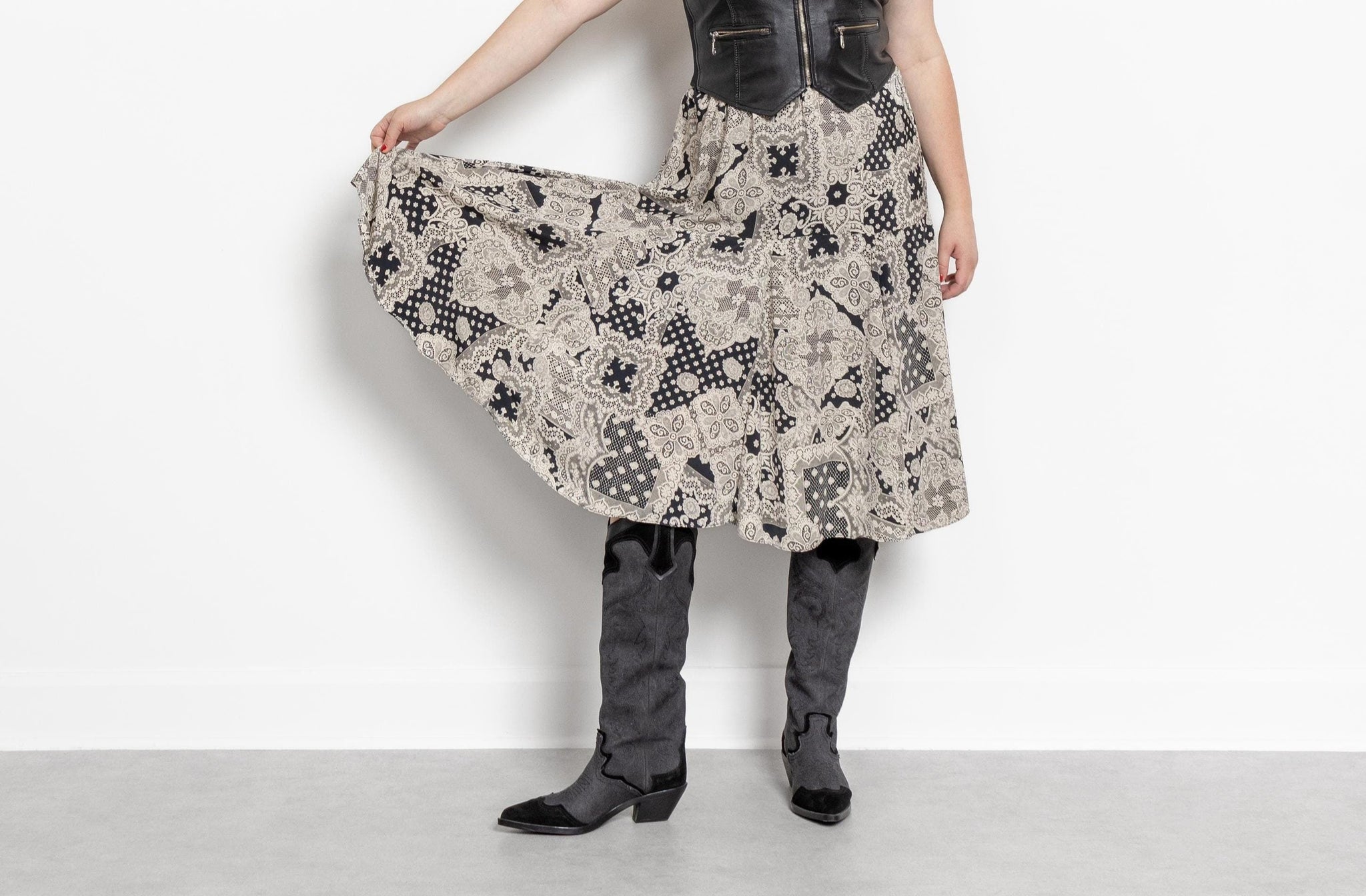 A person wearing a high-waisted midi skirt with a vintage 90's patchwork print in black and white, paired with boots. The skirt has an elastic waistline and is made of a light, soft fabric.