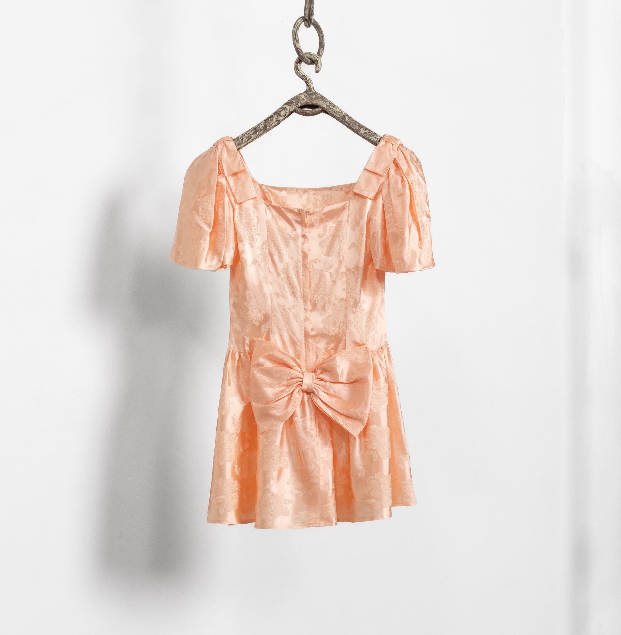Peach-colored dress hanging on a hook against a white background