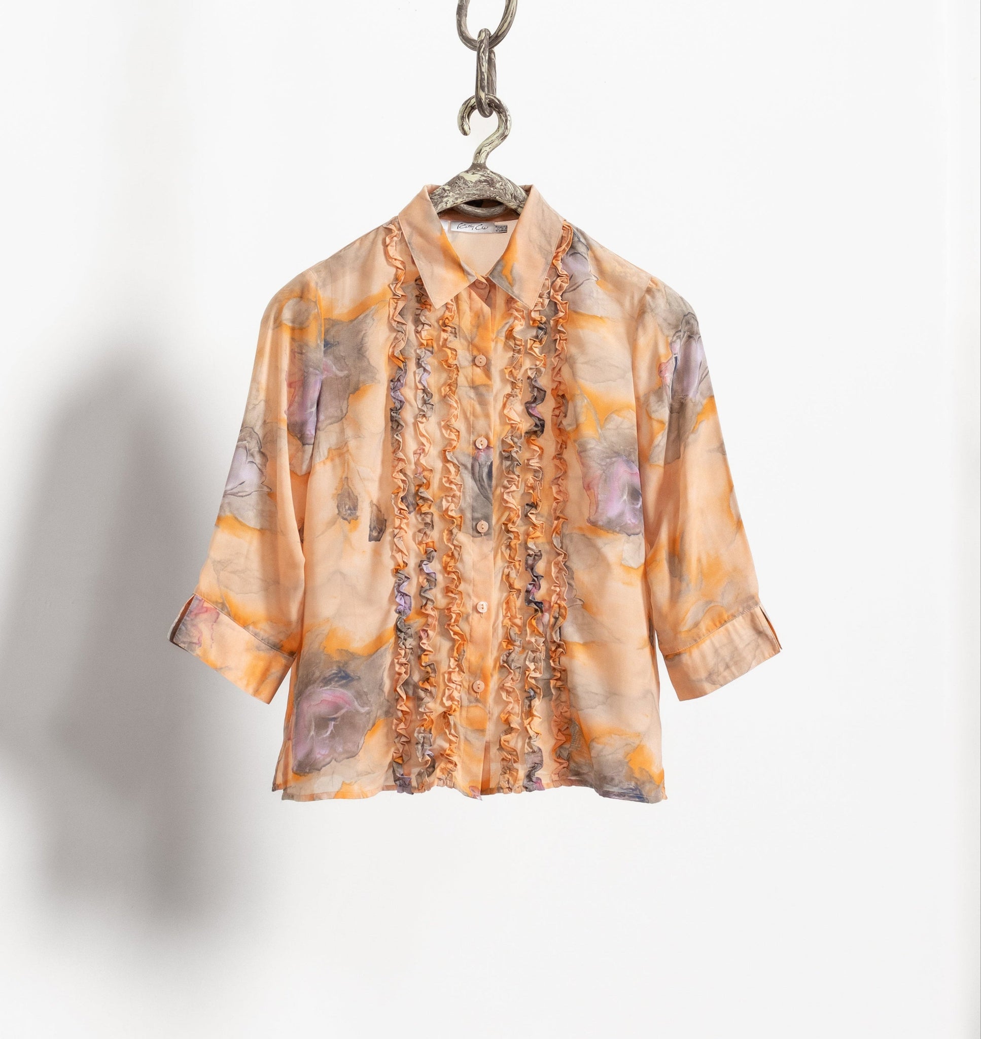 Vintage pastel orange blouse with a watercolor floral pattern and buttons down the front, displayed on a hanger.