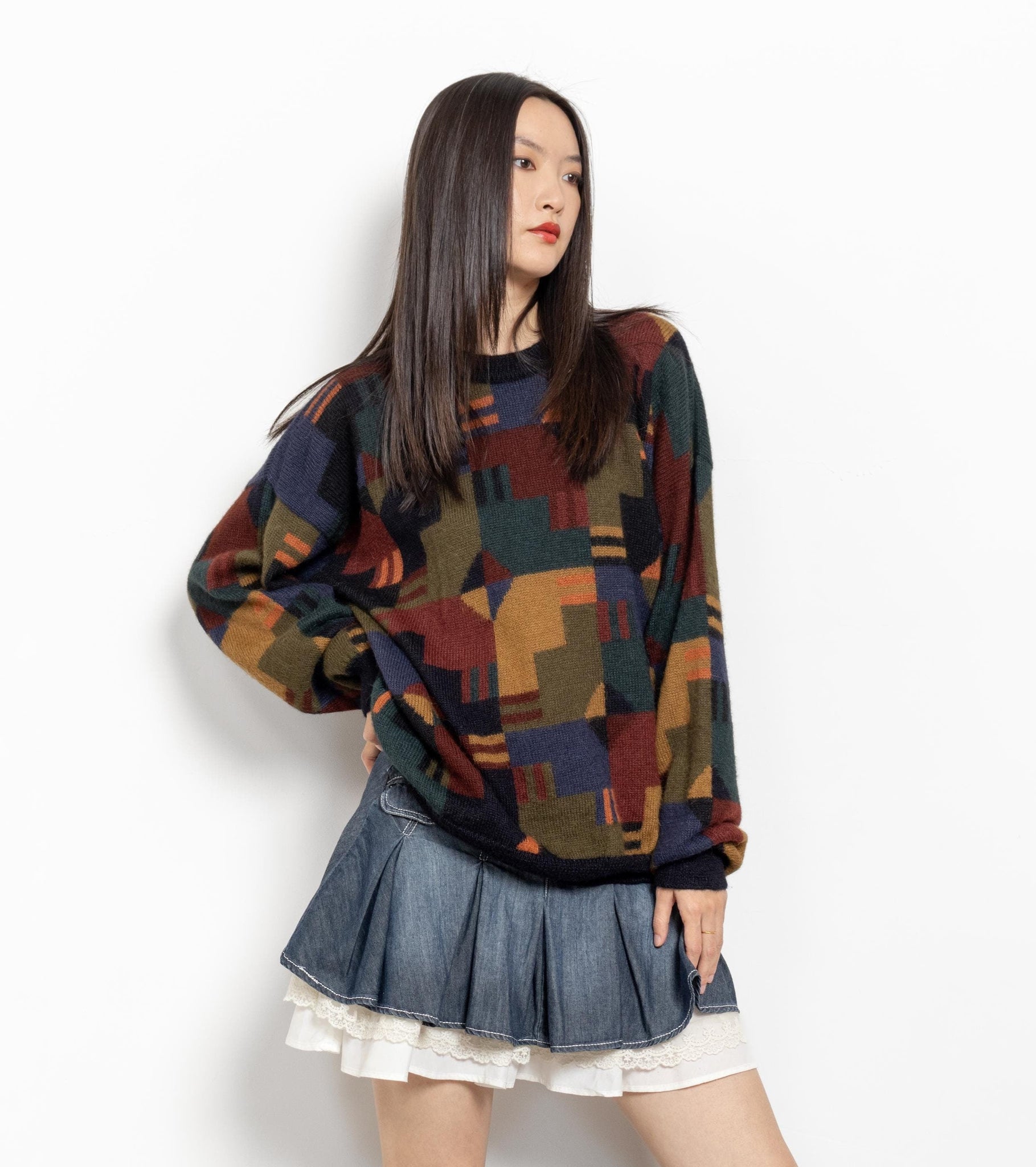 A woman wearing a vintage 90's alpaca pullover with a geometric pattern in multicolor, paired with a denim skirt.