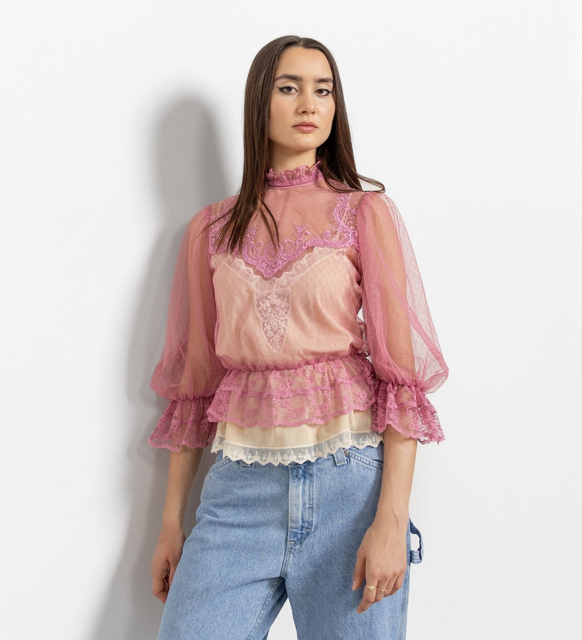 Woman wearing a pink lace top and blue jeans against a white background