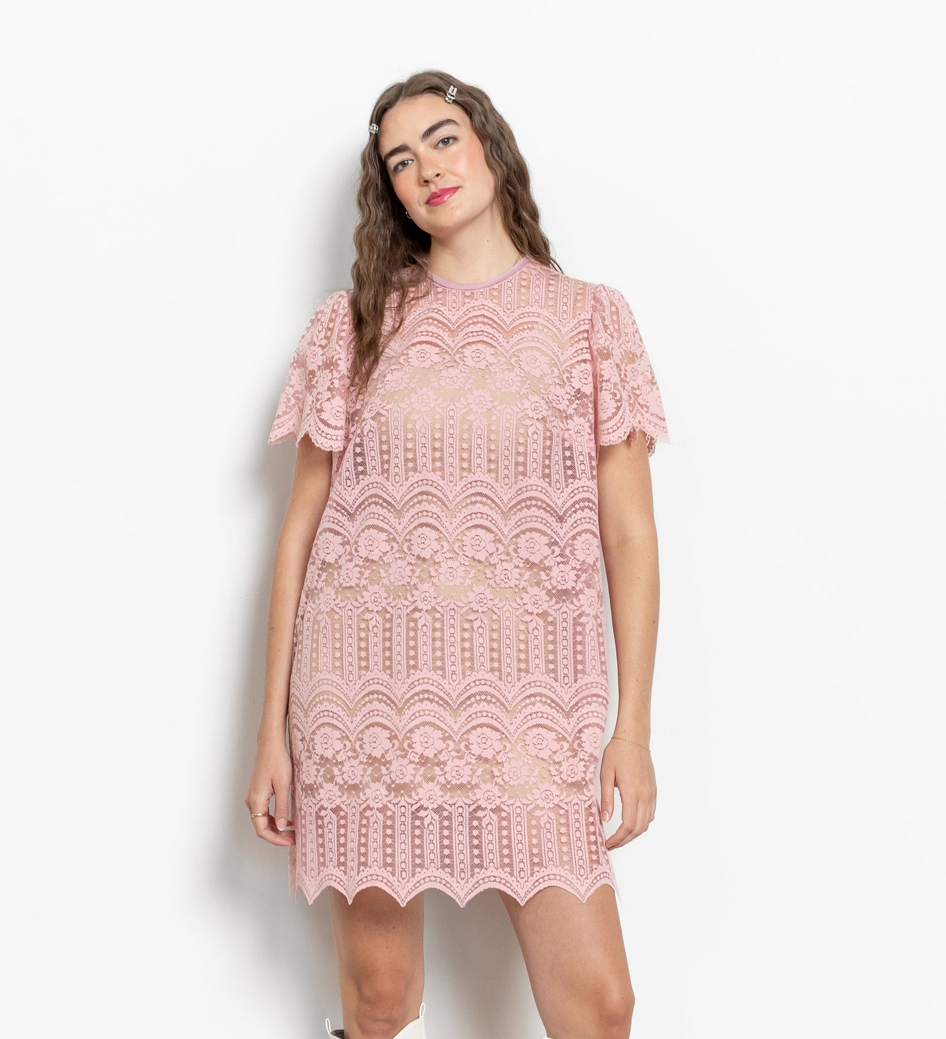 A model wearing a vintage sheer pink lace mini dress with short sleeves and a round neckline.