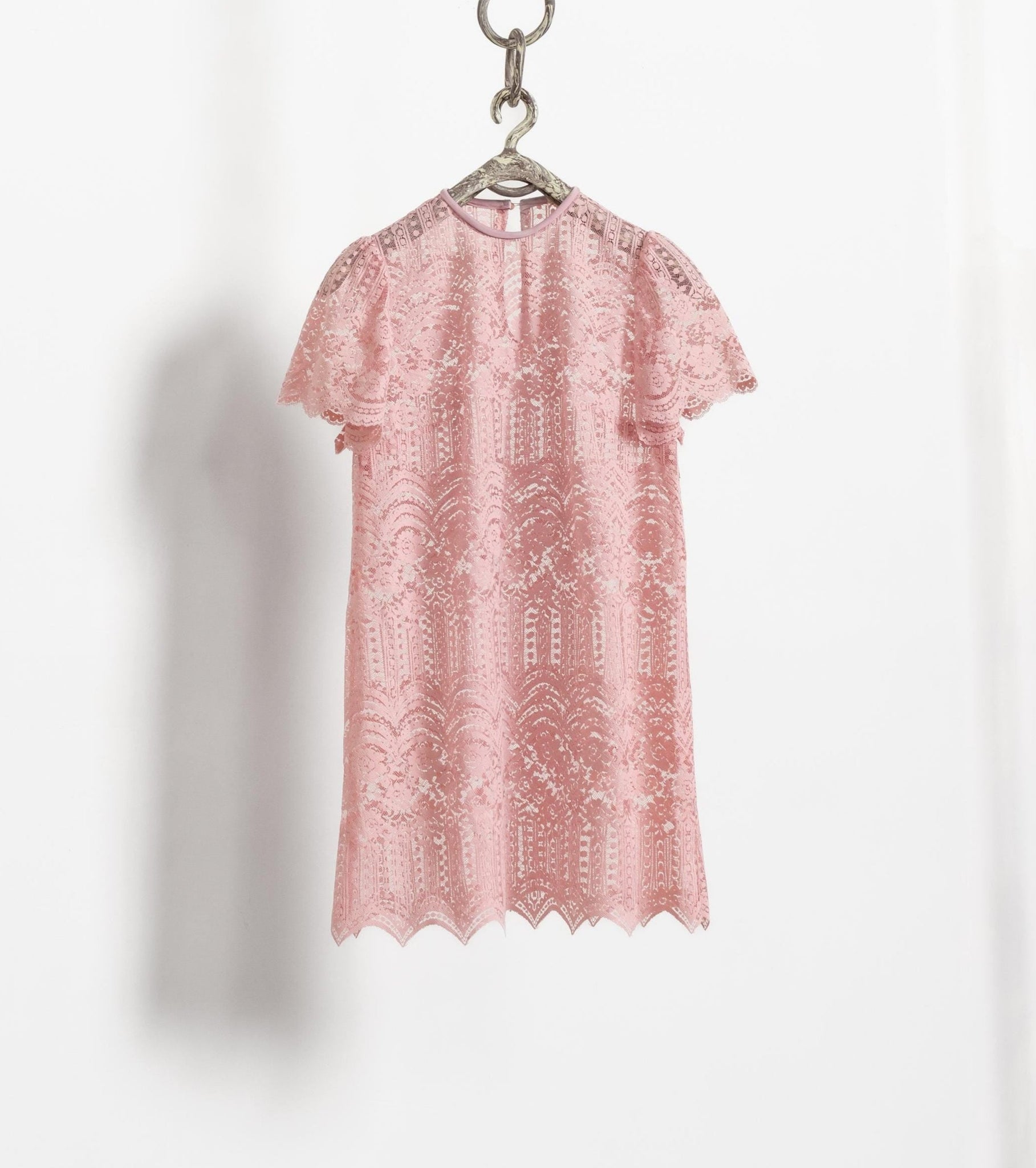 Sheer pink lace mini dress with short sleeves, hung on a hanger against a white wall.