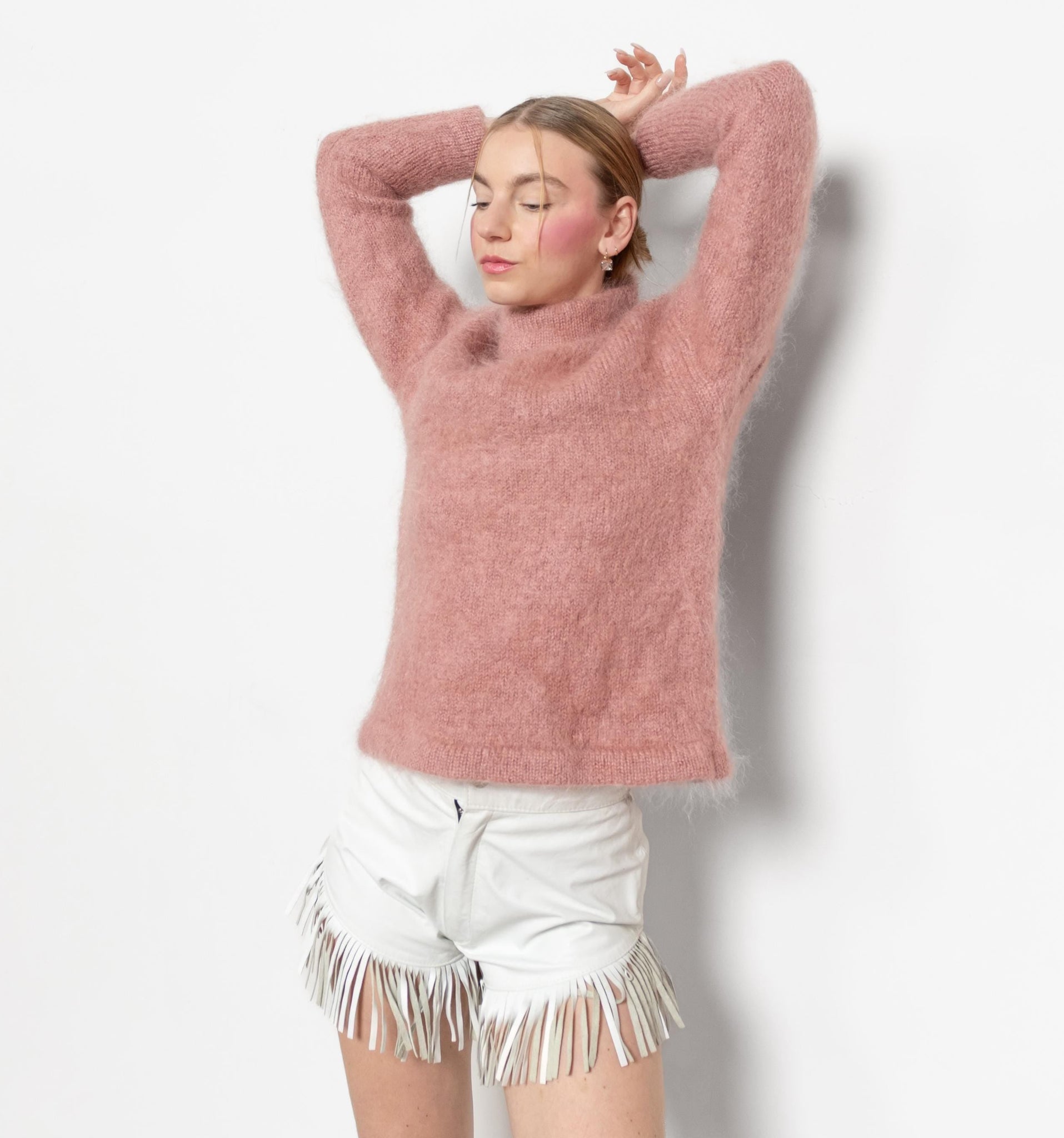 A person wearing a pink mohair-blend pullover jumper with three quarter length sleeves and white shorts with fringes.