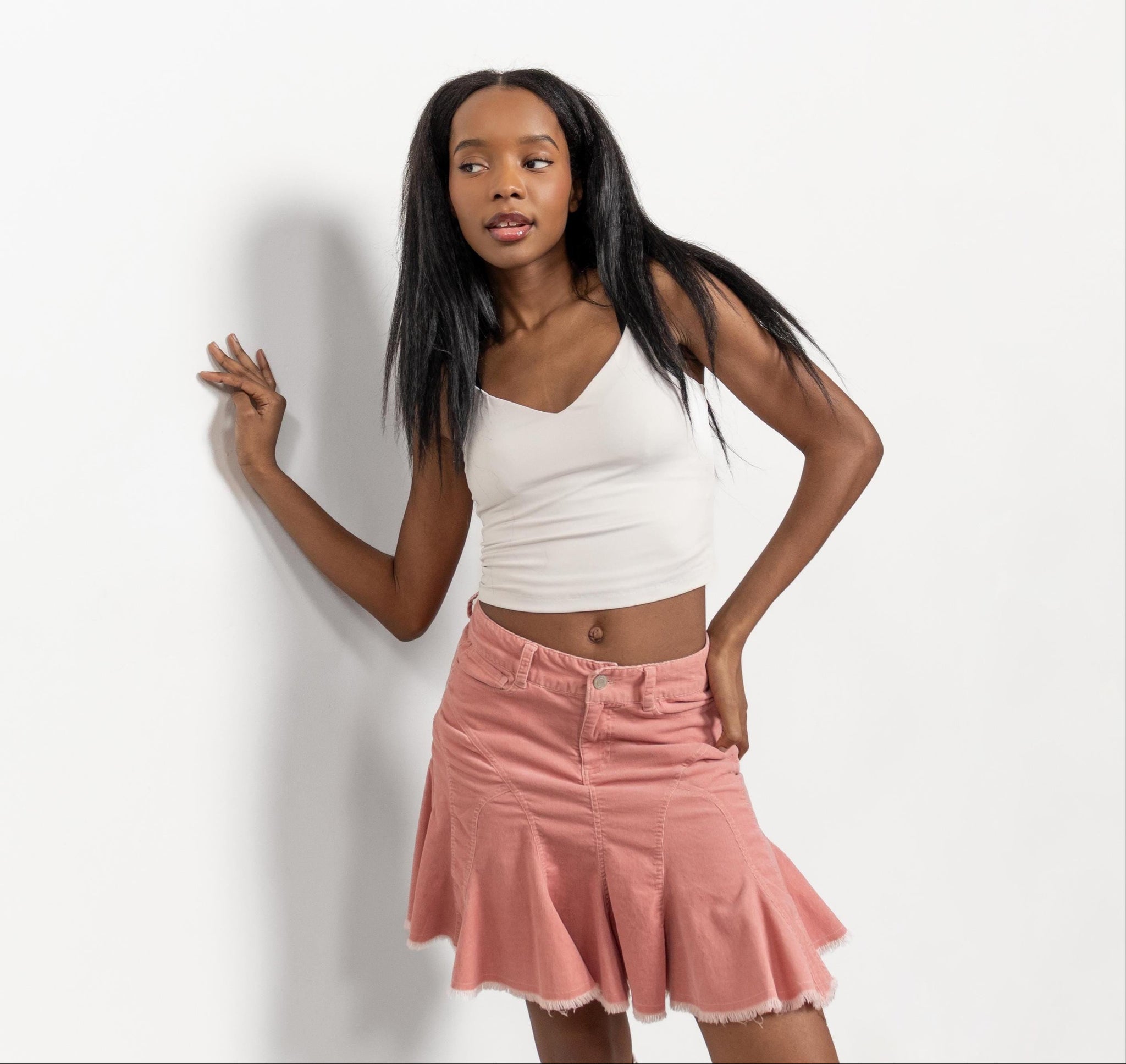 Woman wearing a white top and pink skirt against a plain background