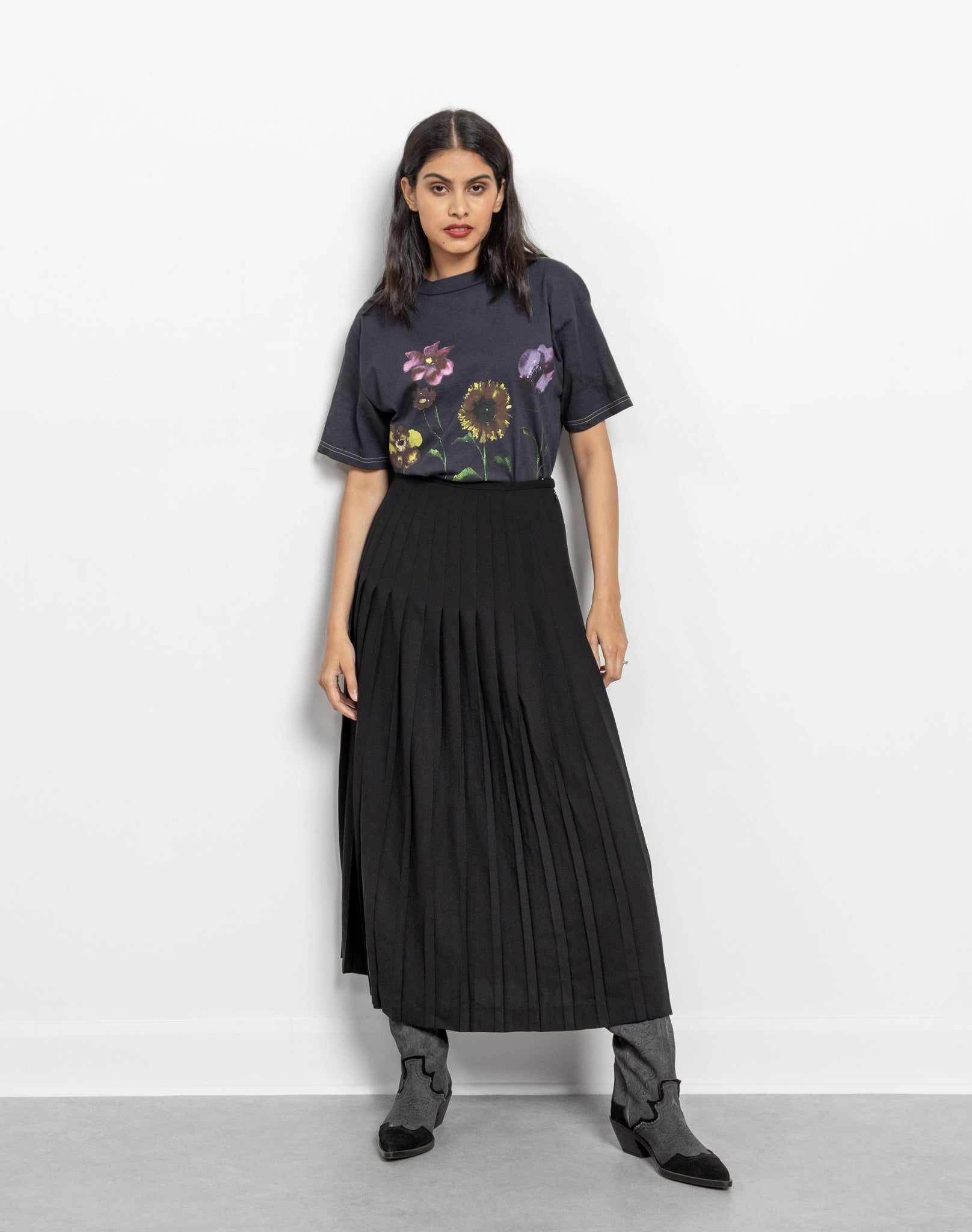 Woman wearing a black t-shirt with floral design and a long black pleated skirt on a white background