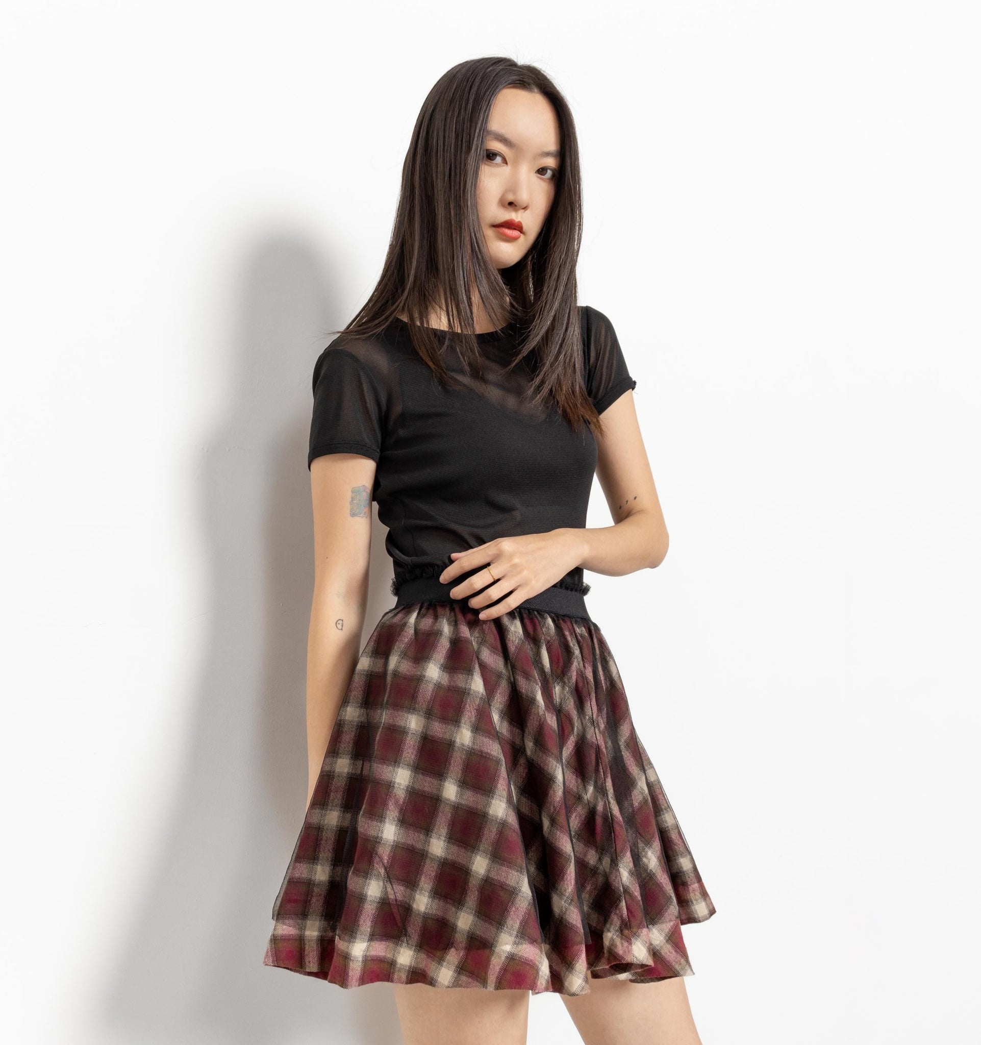 Woman wearing a black top and plaid skirt against a white background