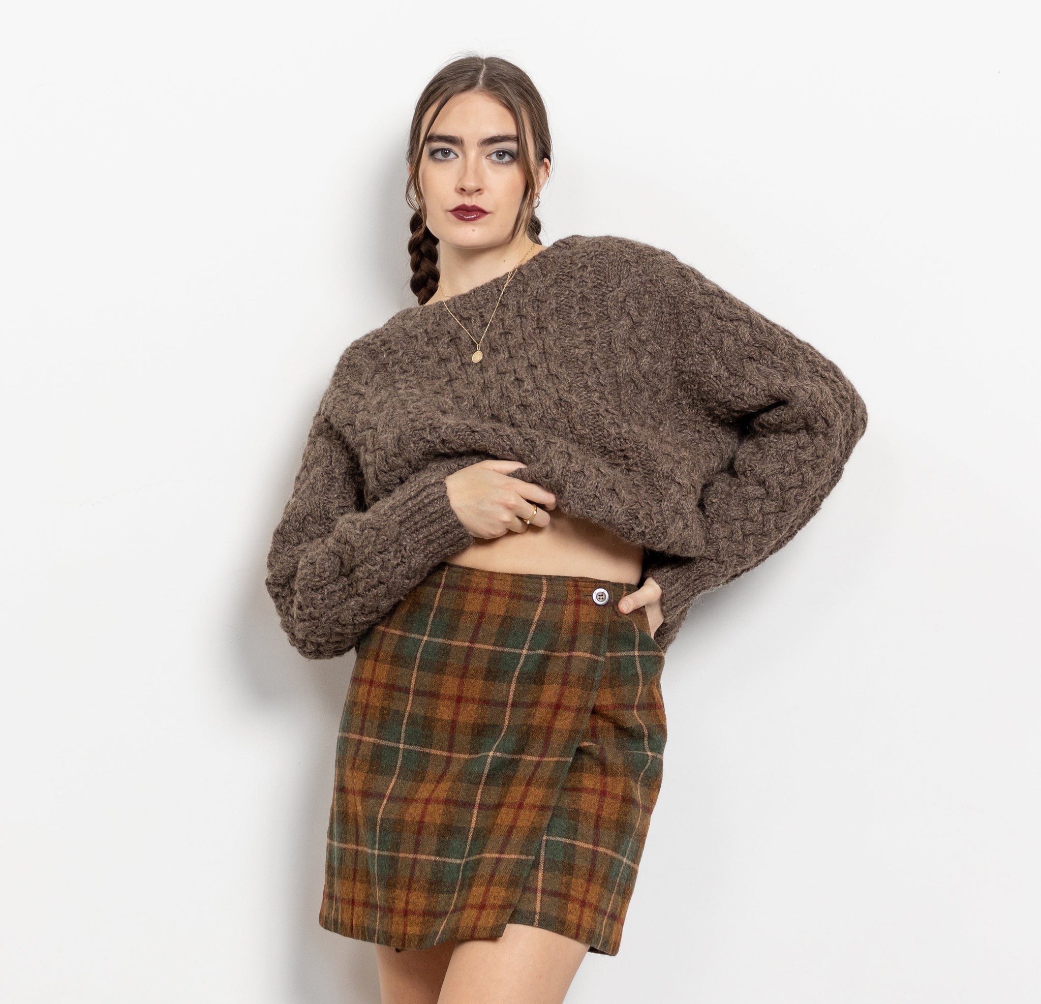 Woman wearing a brown sweater and plaid skirt on a white background