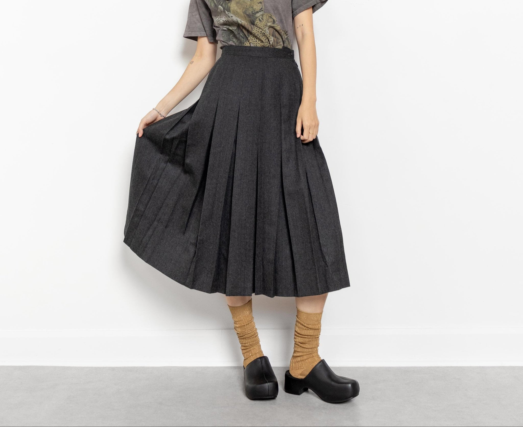 Woman wearing a gray t-shirt with a graphic design and a black pleated skirt on a white background