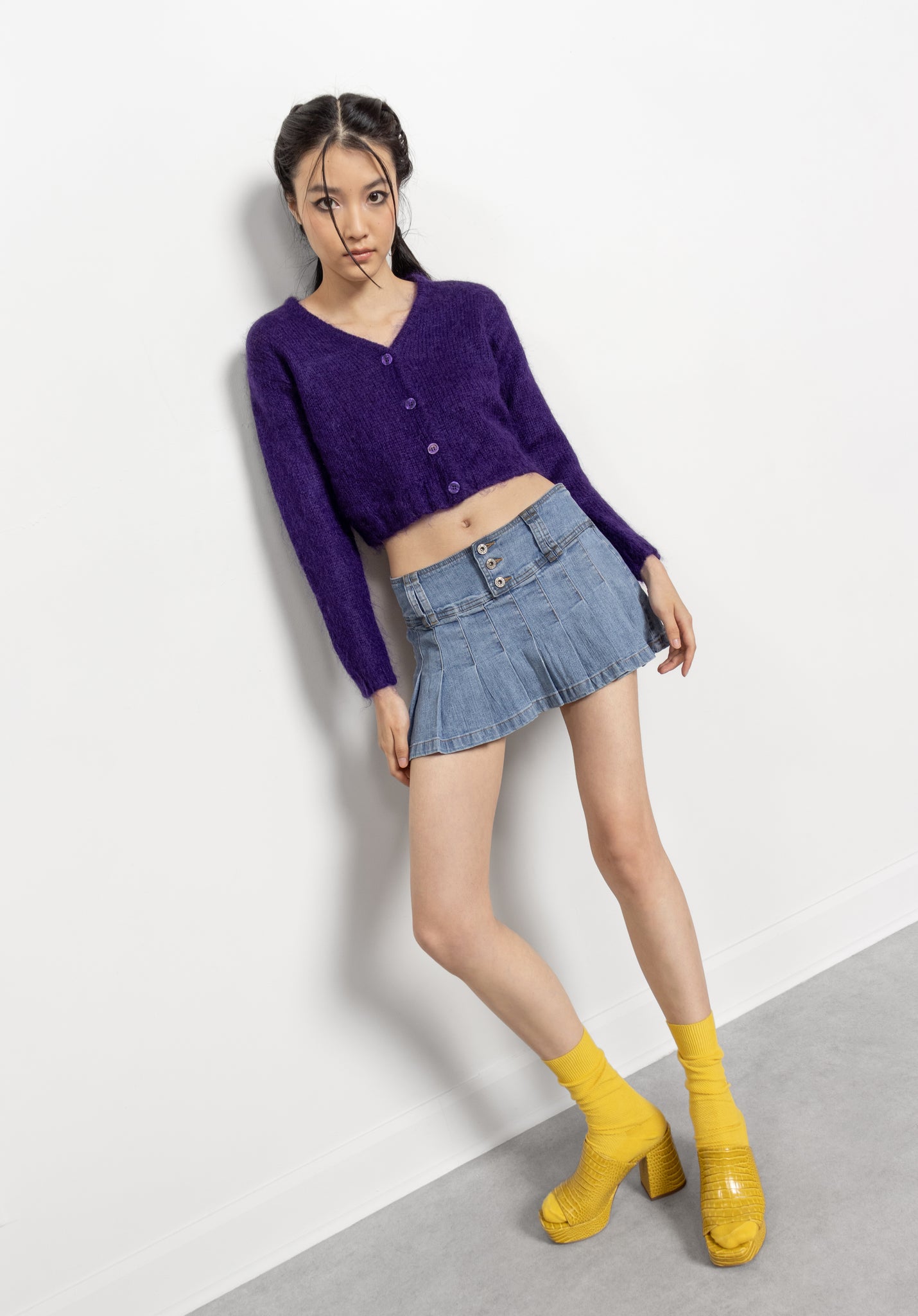 Woman wearing a purple cardigan, denim skirt, and yellow shoes on a white background
