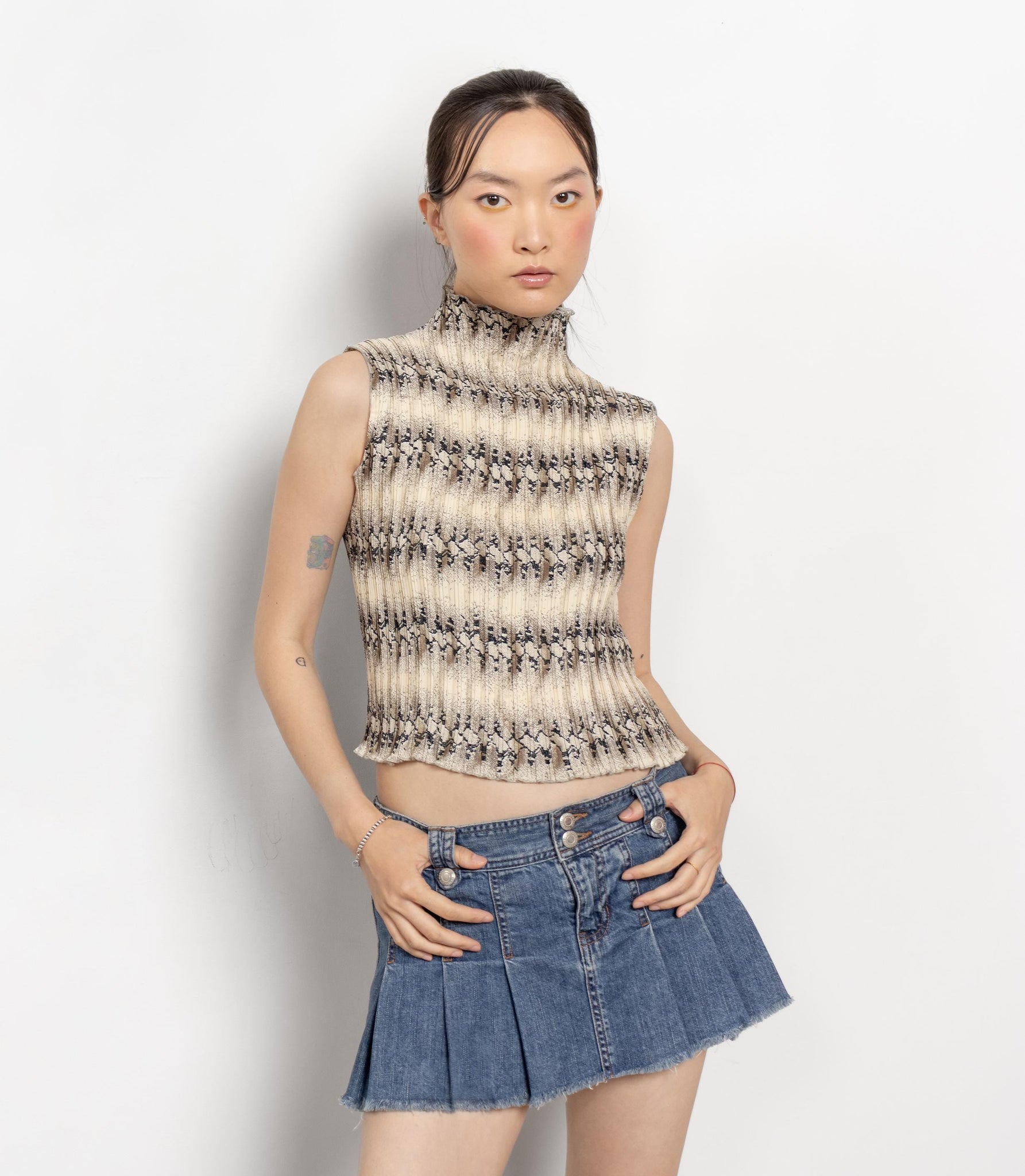 Woman wearing a patterned sleeveless top and denim skirt on a white background