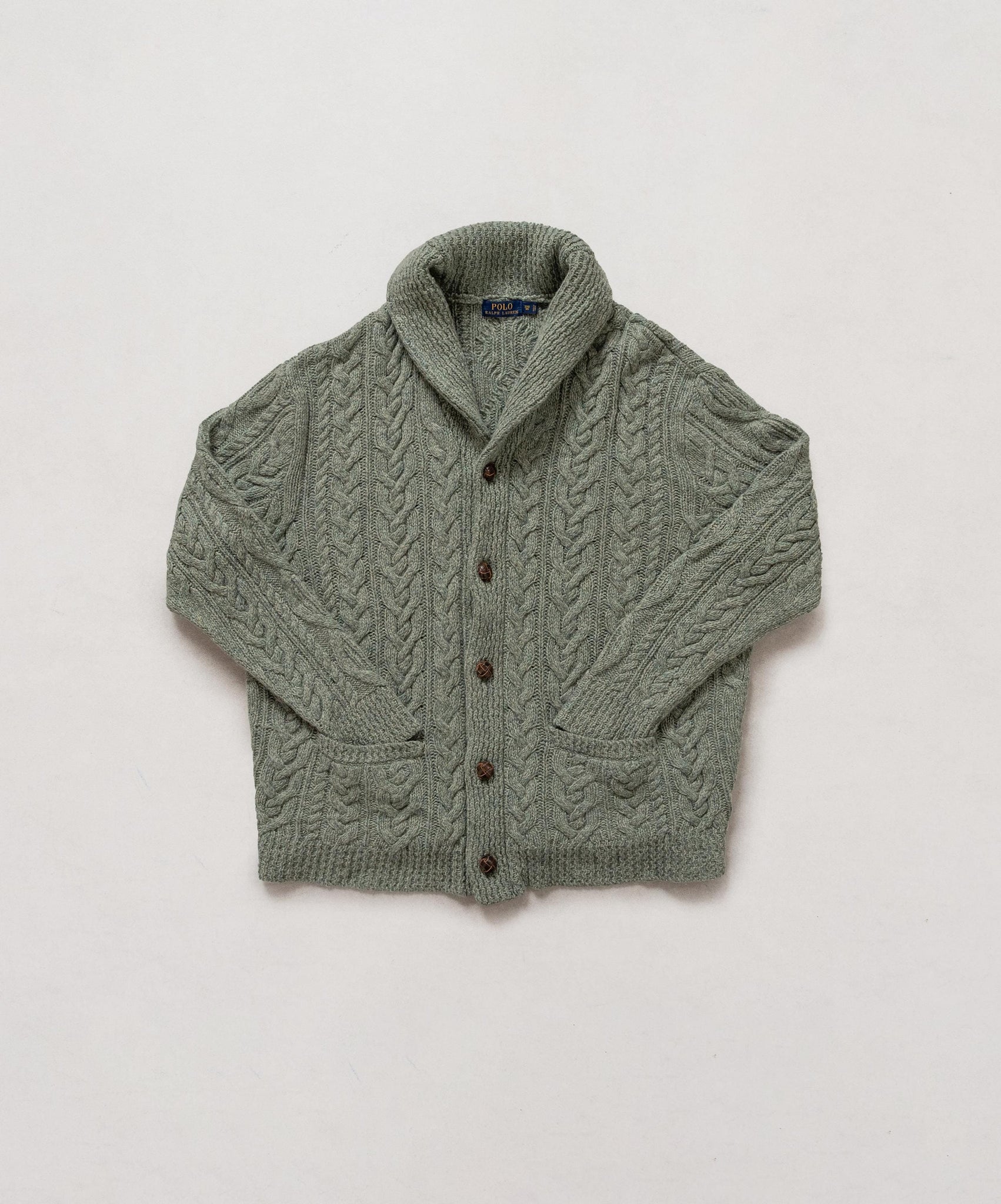 Green knitted cardigan with brown buttons on a light gray background