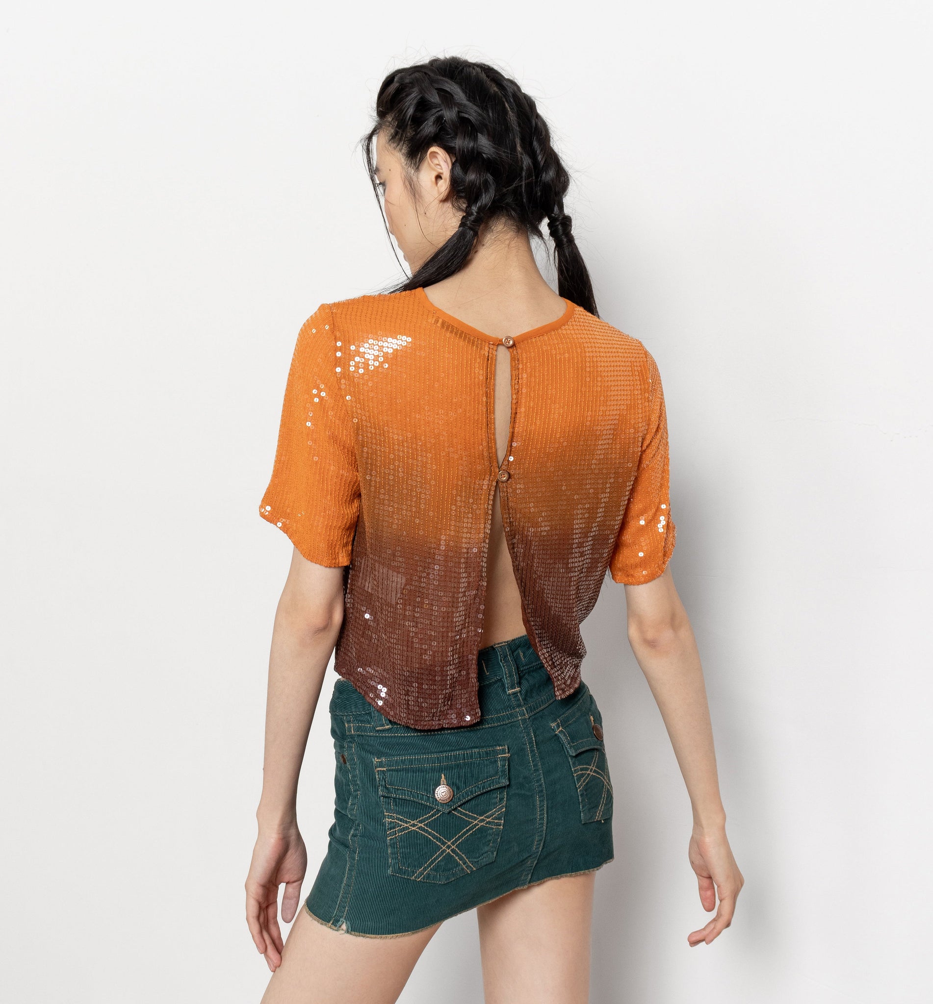 Woman wearing an orange sequin top and green denim skirt on a white background