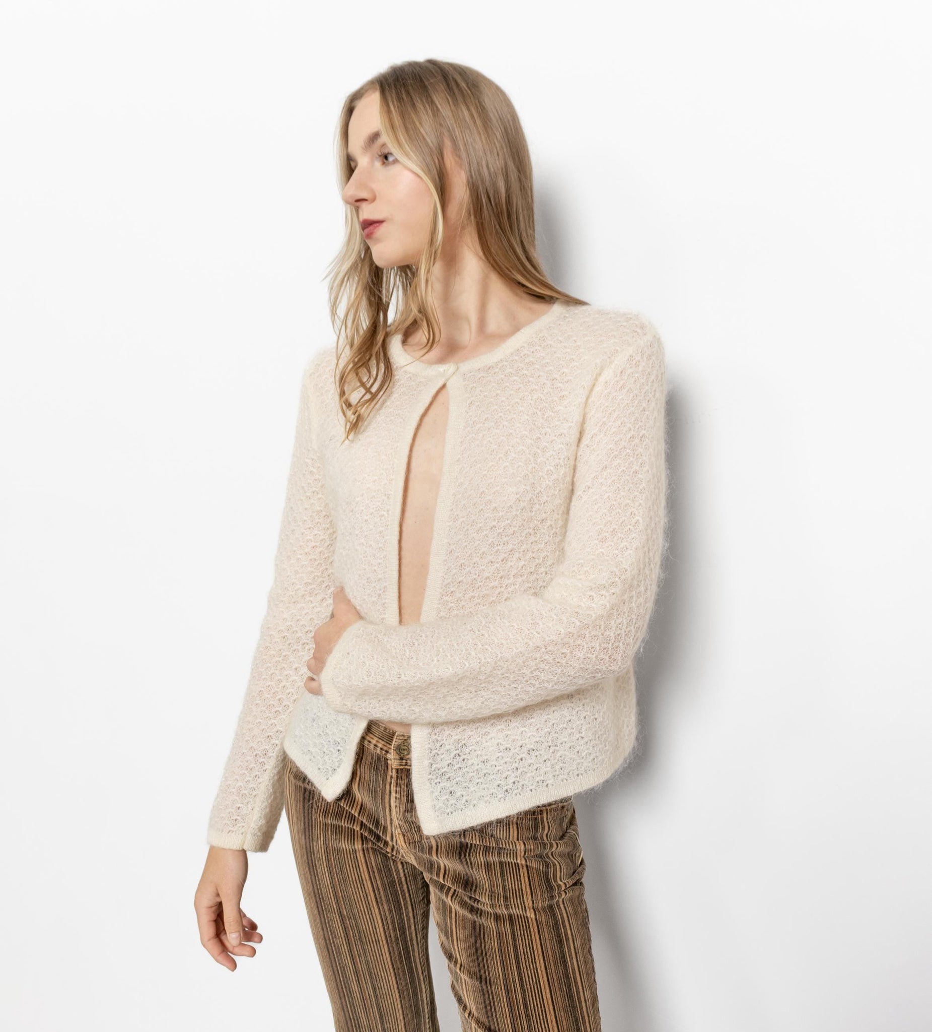 Woman wearing a beige cardigan over a sheer top with plaid pants on a white background