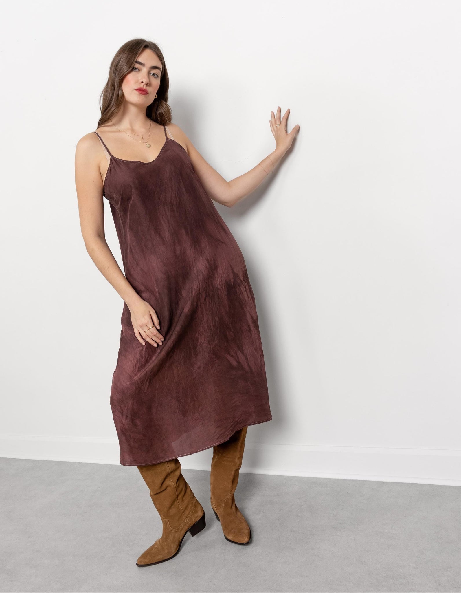 Woman wearing a brown slip dress and boots against a white background