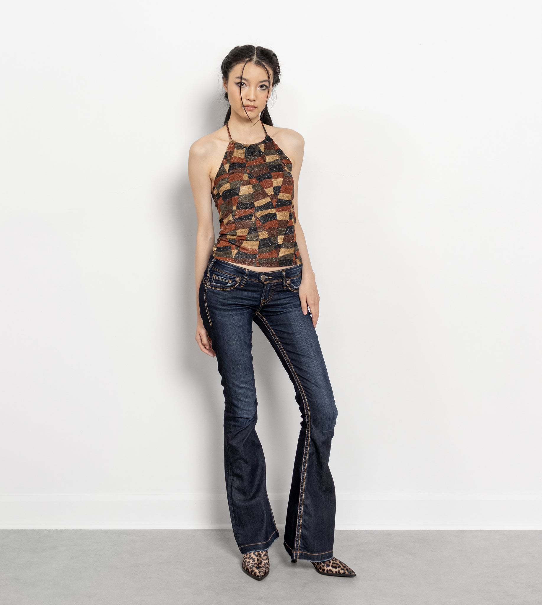 Woman wearing a patterned top and blue jeans against a white background