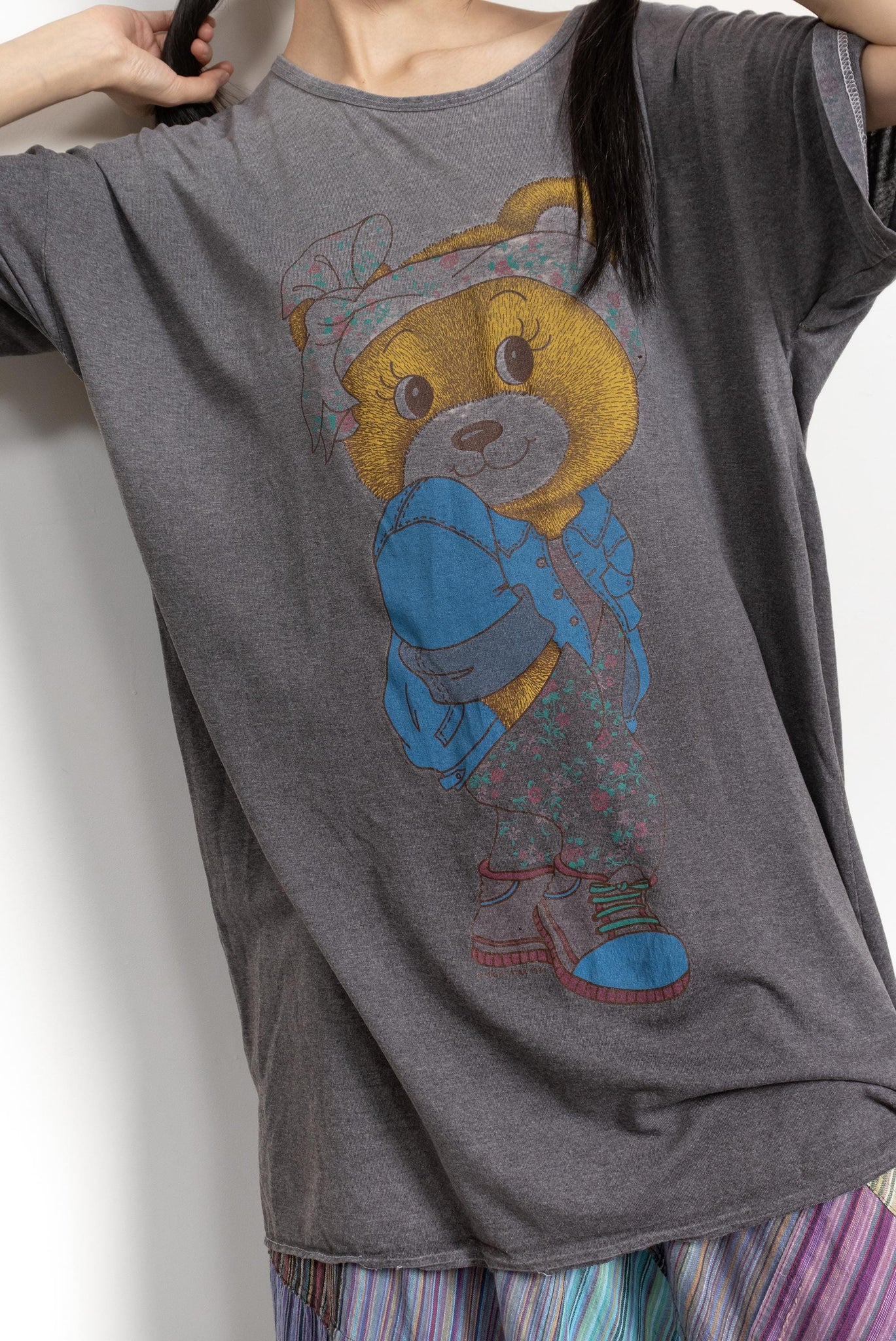 Person wearing a gray t-shirt with a teddy bear graphic on a plain background