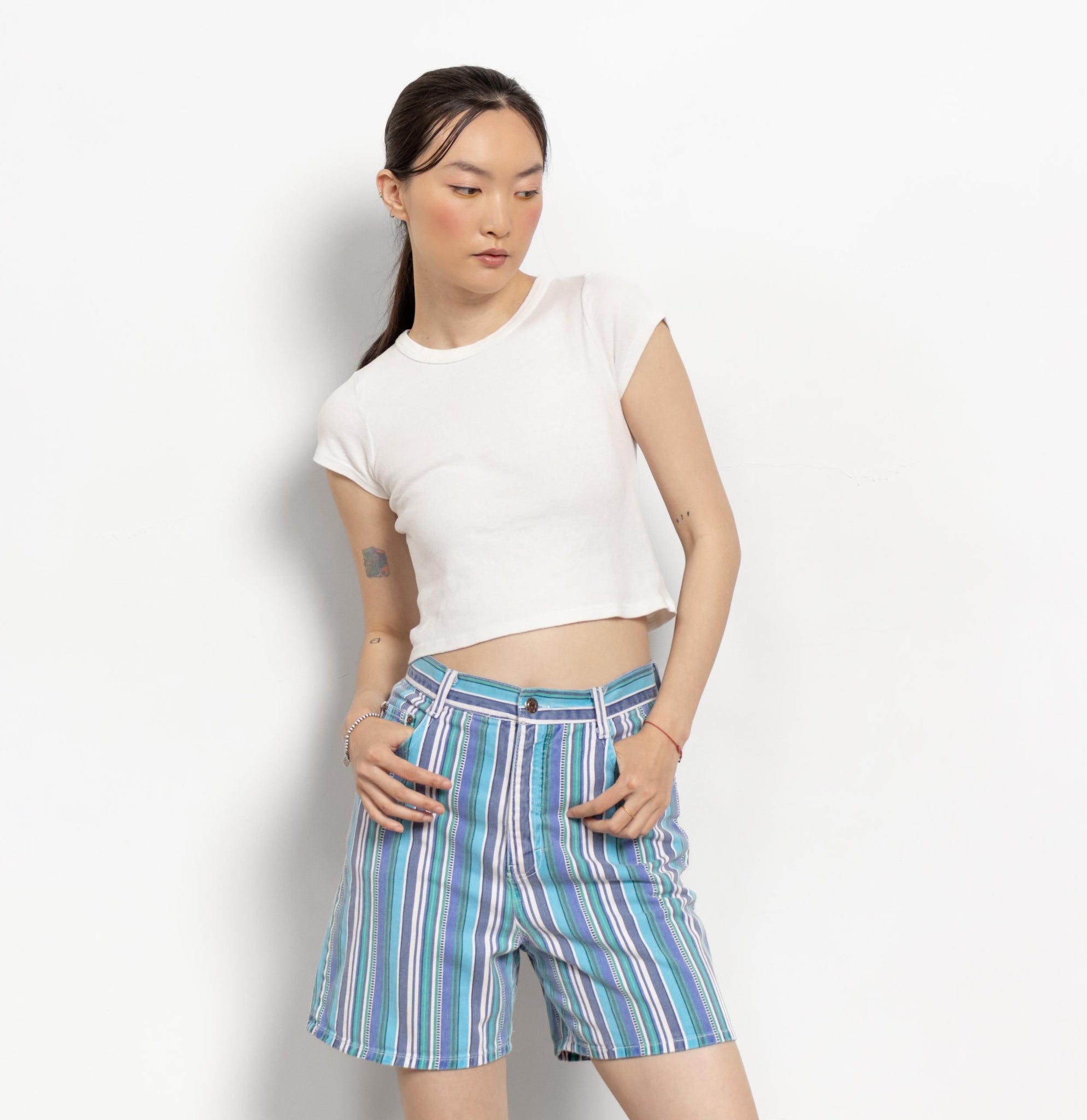 Woman wearing a white crop top and striped shorts on a plain background